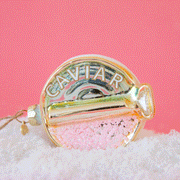 On a pink background is a gold, pink and light blue caviar tin ornament with light pink beads on one side and white and gold text on the other that reads, "CAVIAR".