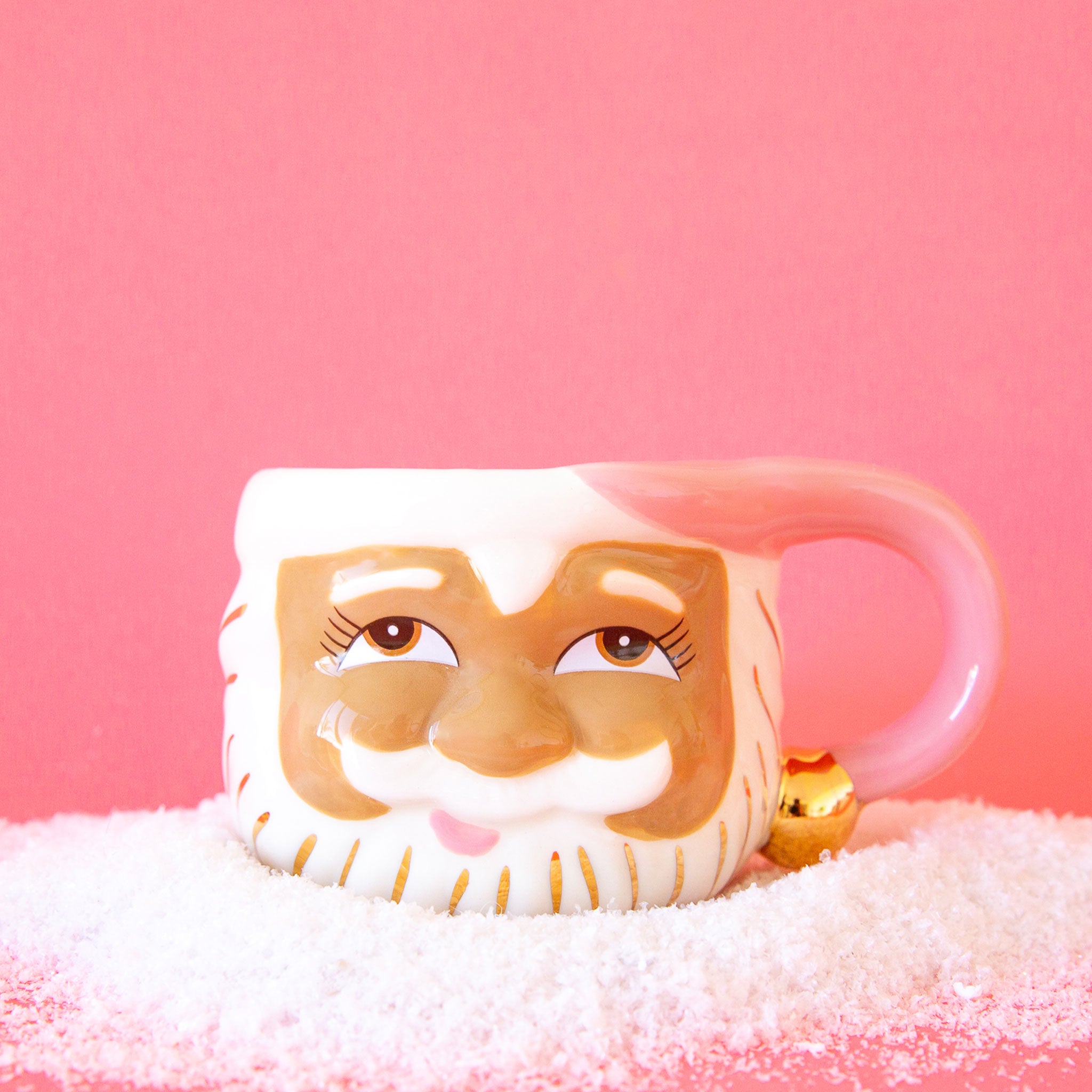 On a pink background is a santa face ceramic mug with a pink handle.