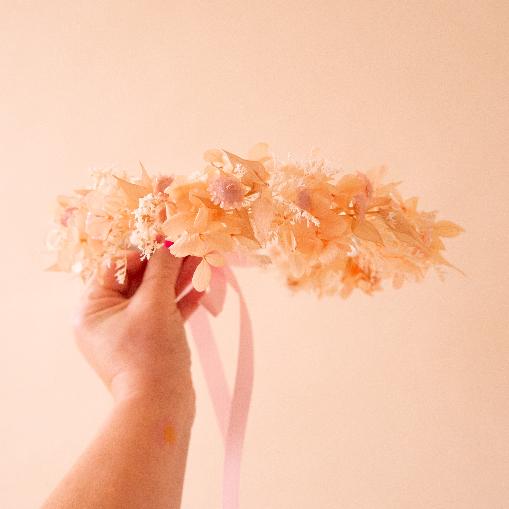 A neutral dried floral flower crown with a pink ribbon tie. 