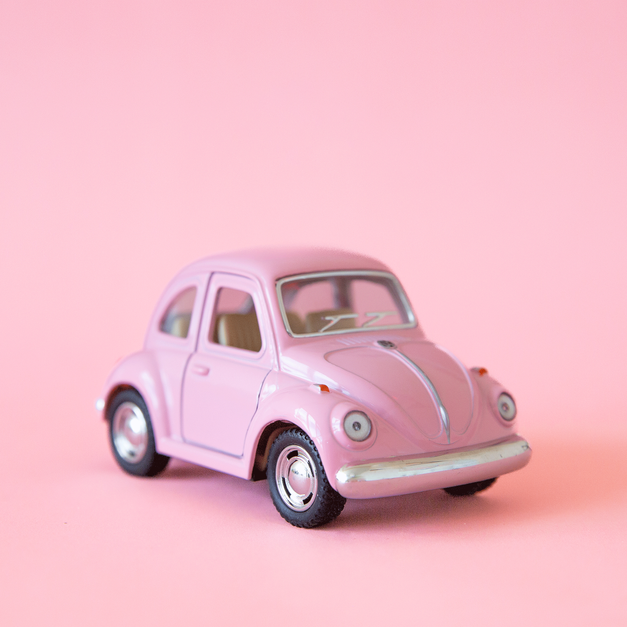 On a pink background is a pink VW bug shaped toy car. 