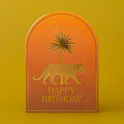 An orange arched card with gold foiled text that reads, "May This Year Be As Magnificent As You Happy Birthday" along with a gold foiled leopard design. 