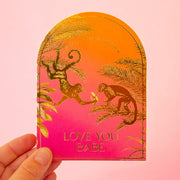 A pink and orange ombre arched shape card with gold foiled monkey illustrations and gold text that reads, "You Put The Ass In Potassium Love You Babe".