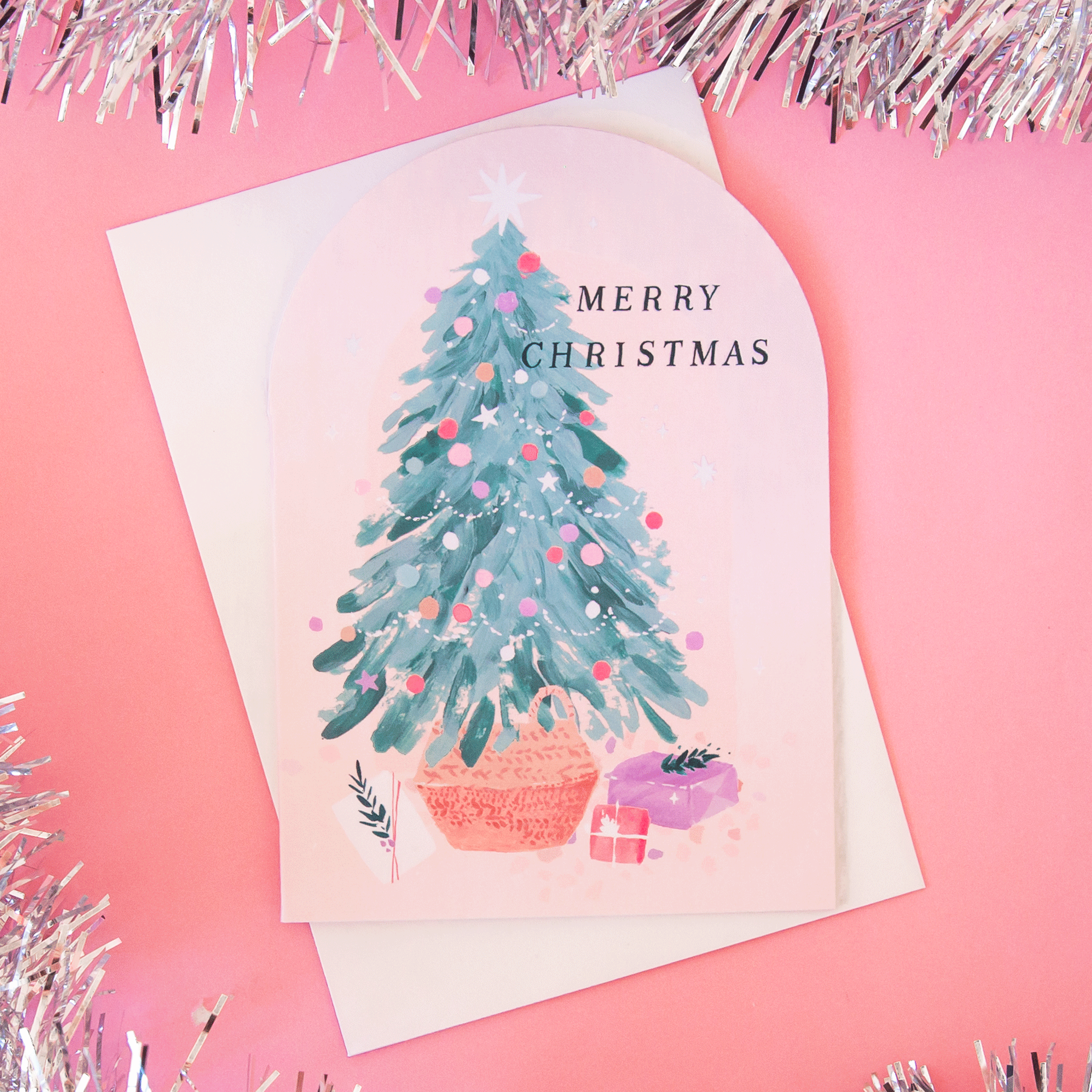 On a pink background is a pink arched card with a Christmas tree and black text that reads, "Merry Christmas".