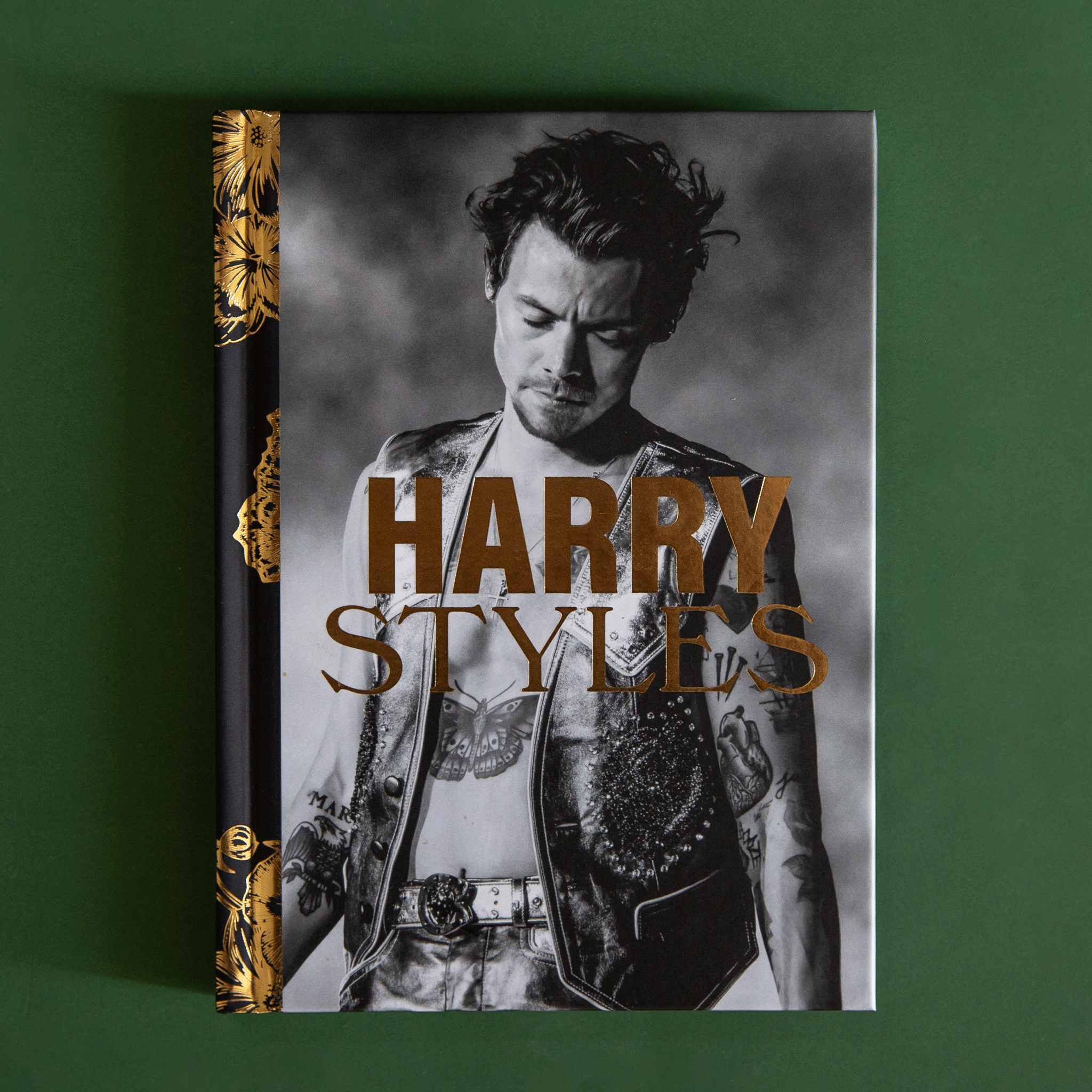 On a green background is a grey book cover with a photo of Harry Styles and gold text that reads, "Harry Styles".