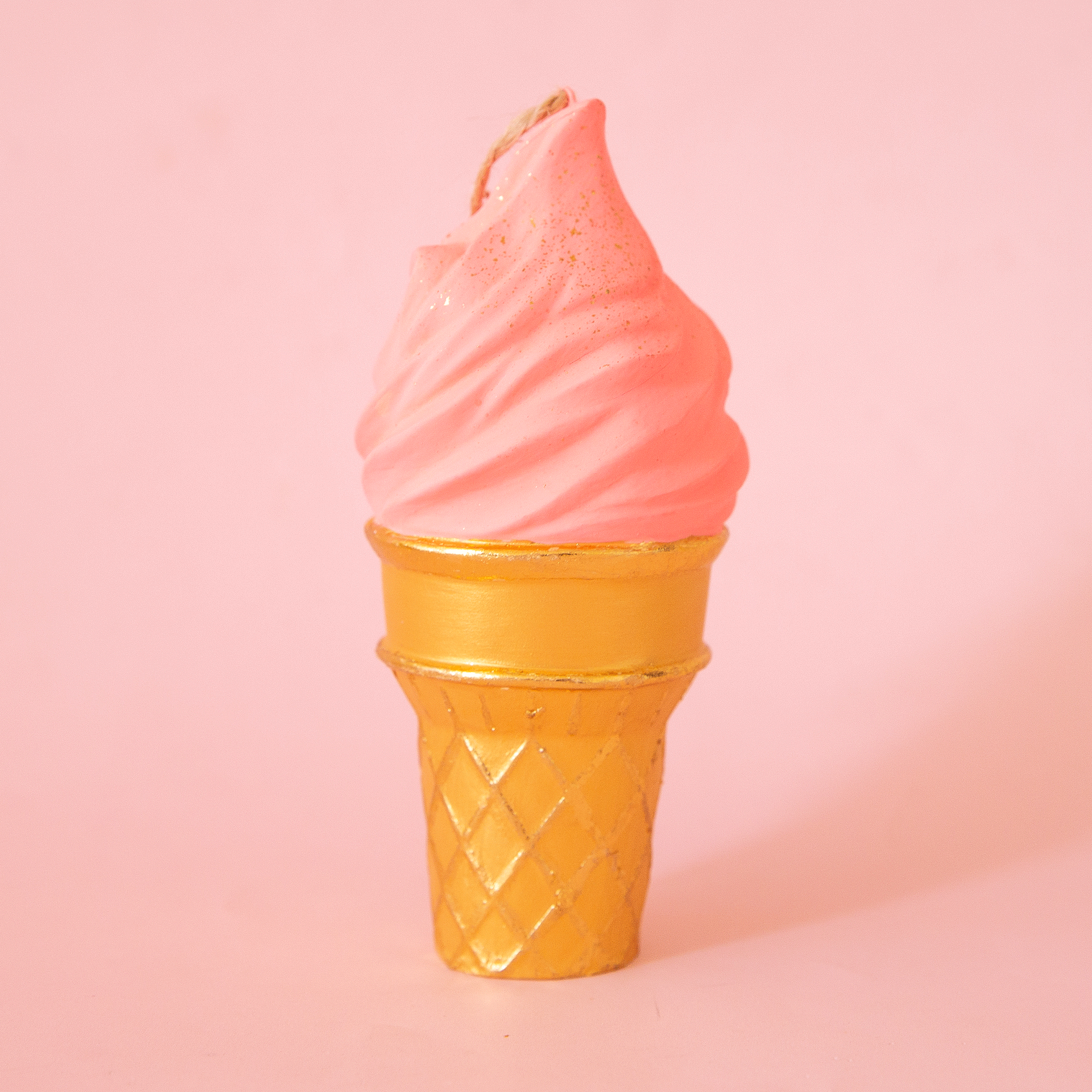 On a pink background is a dark peach ice cream cone shaped ornament.