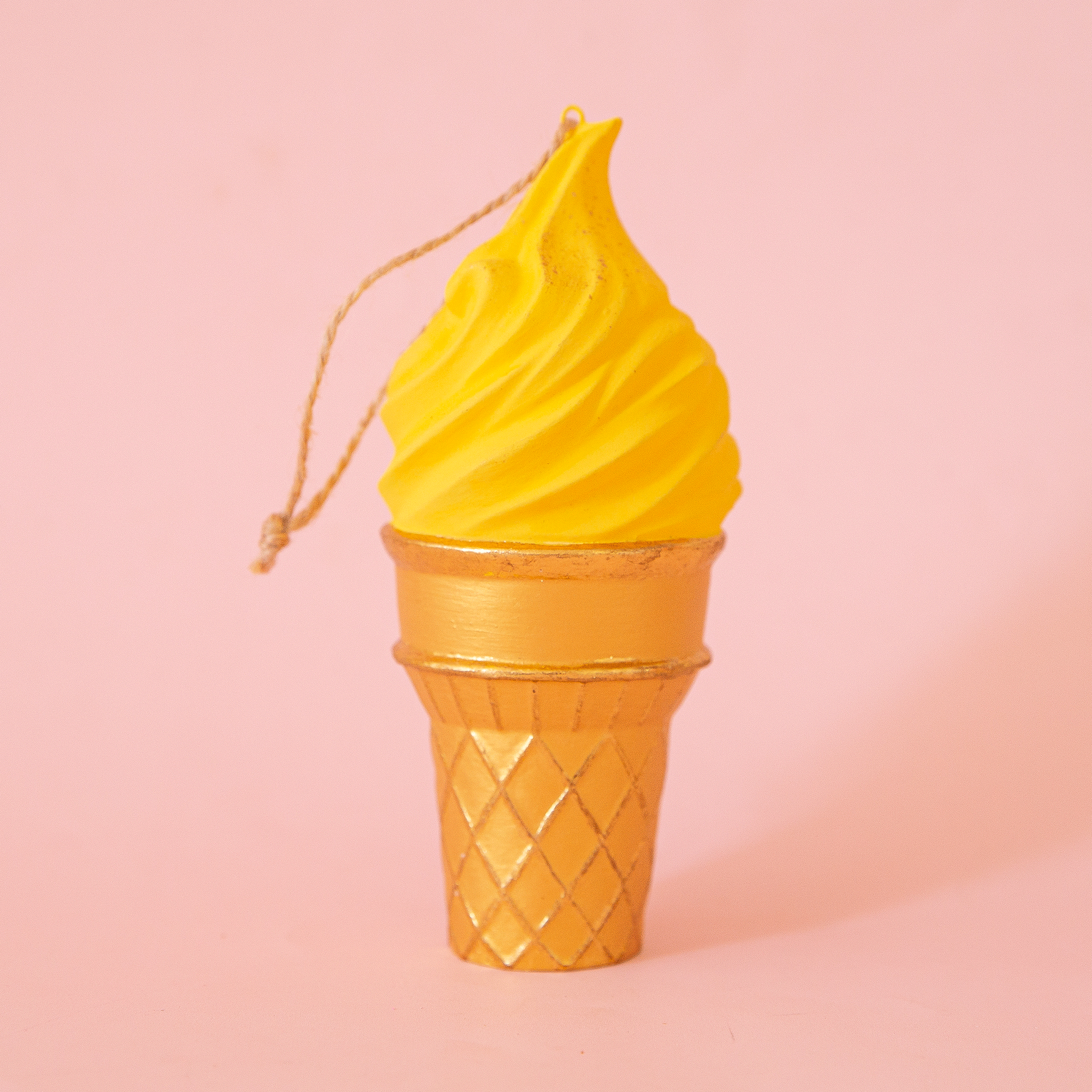 On a pink background is a yellow ice cream cone shaped ornament. 