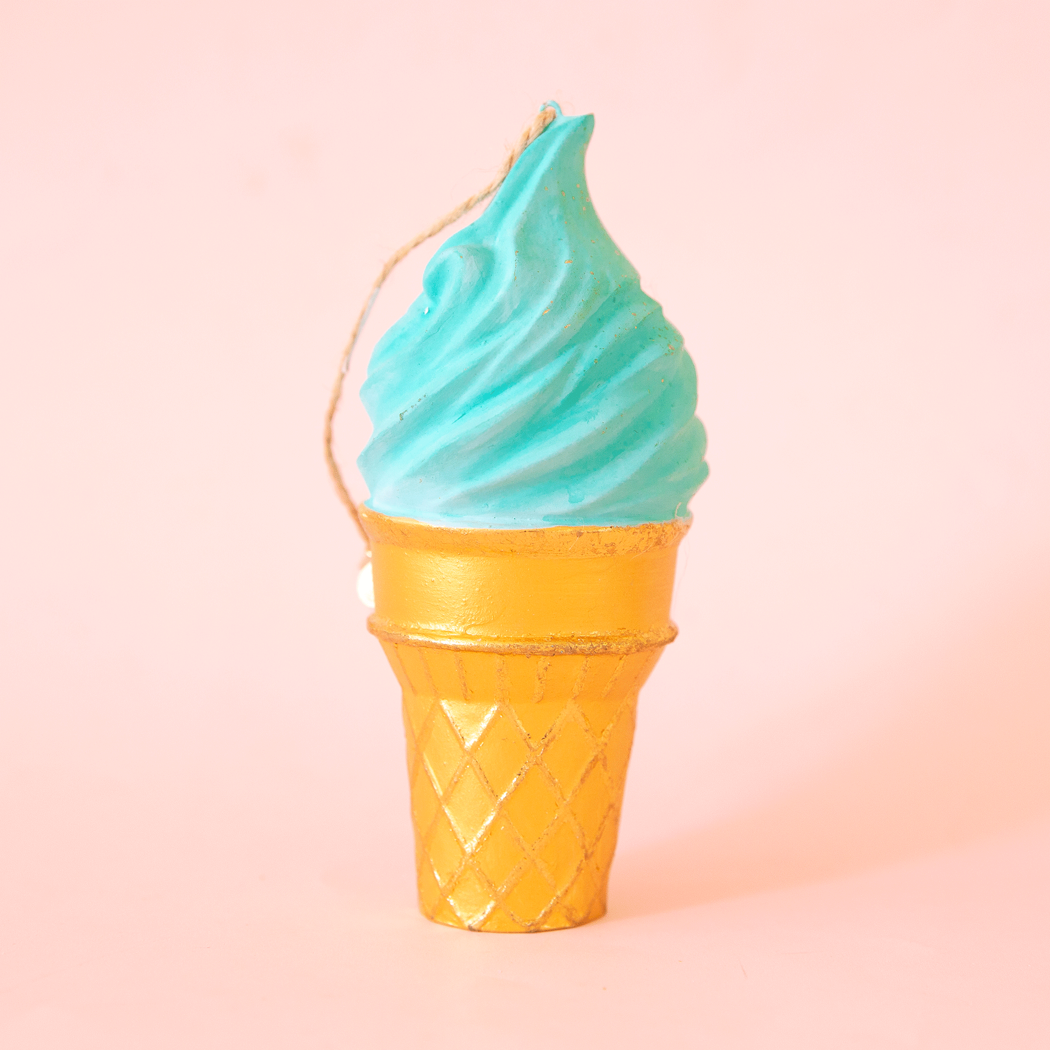 On a light pink background is an ice cream cone shaped ornament with a turquoise blue "ice cream". 