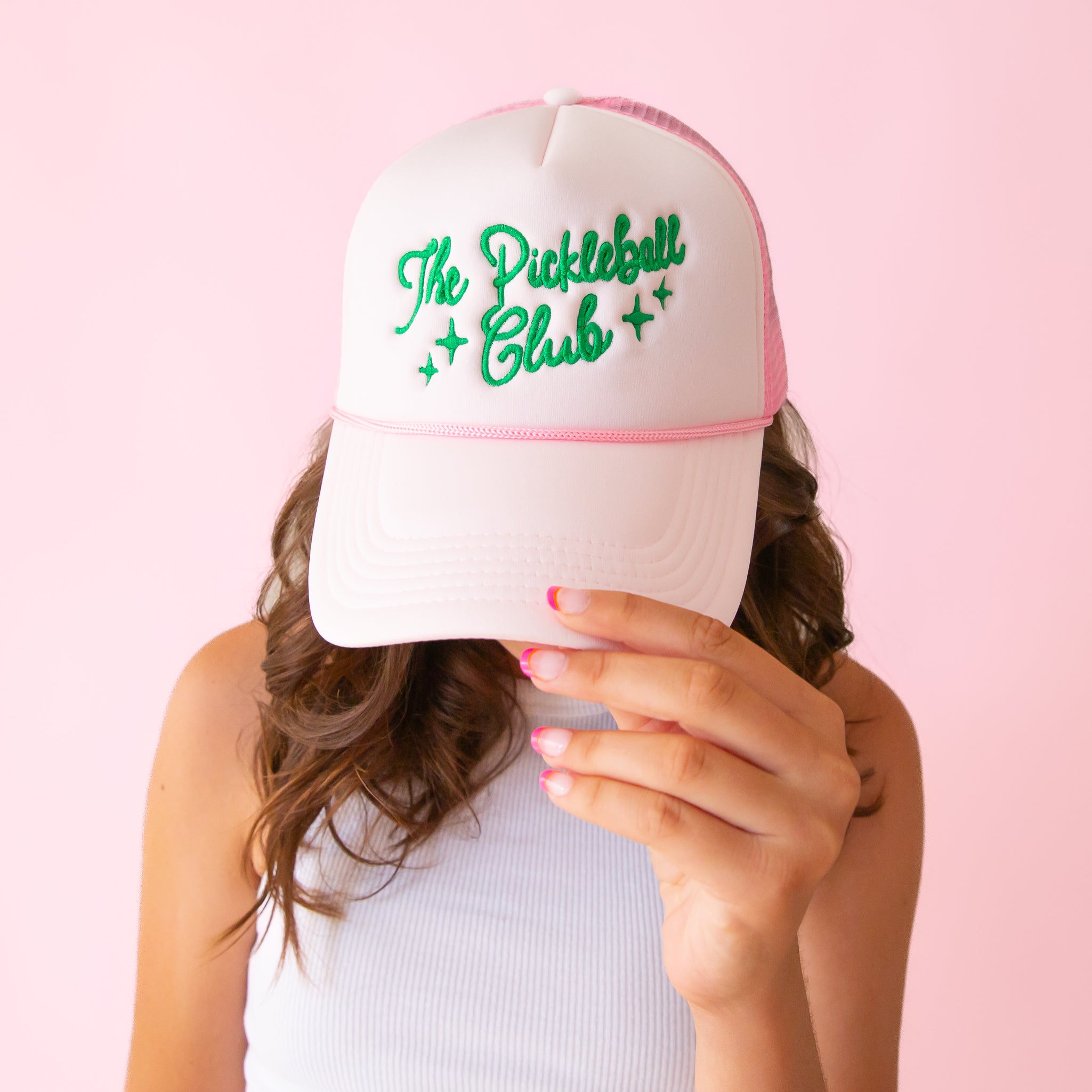 A light pink trucker hat with green embroidered text across the front that reads, &quot;The Pickleball Club&quot;.