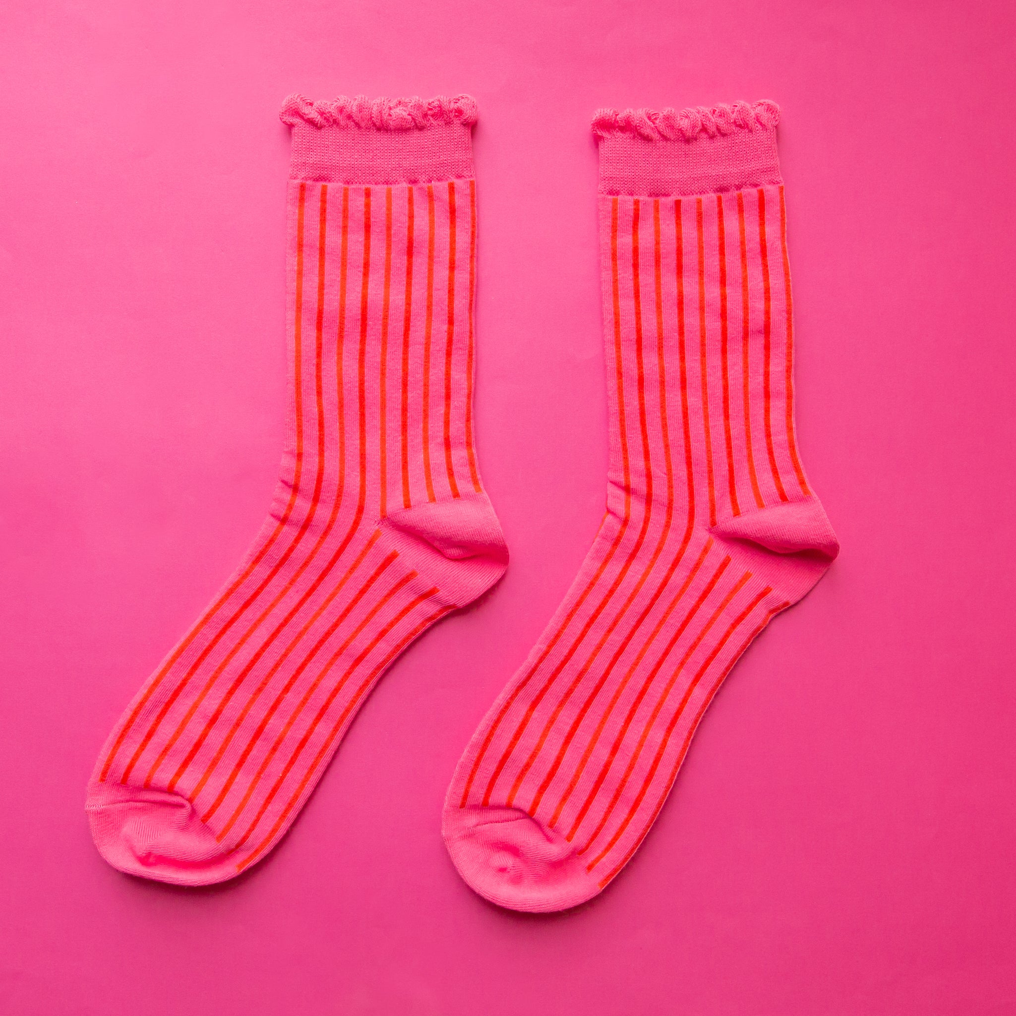 A pair of fuchsia colored striped socks with a ruffle detail at the top. 