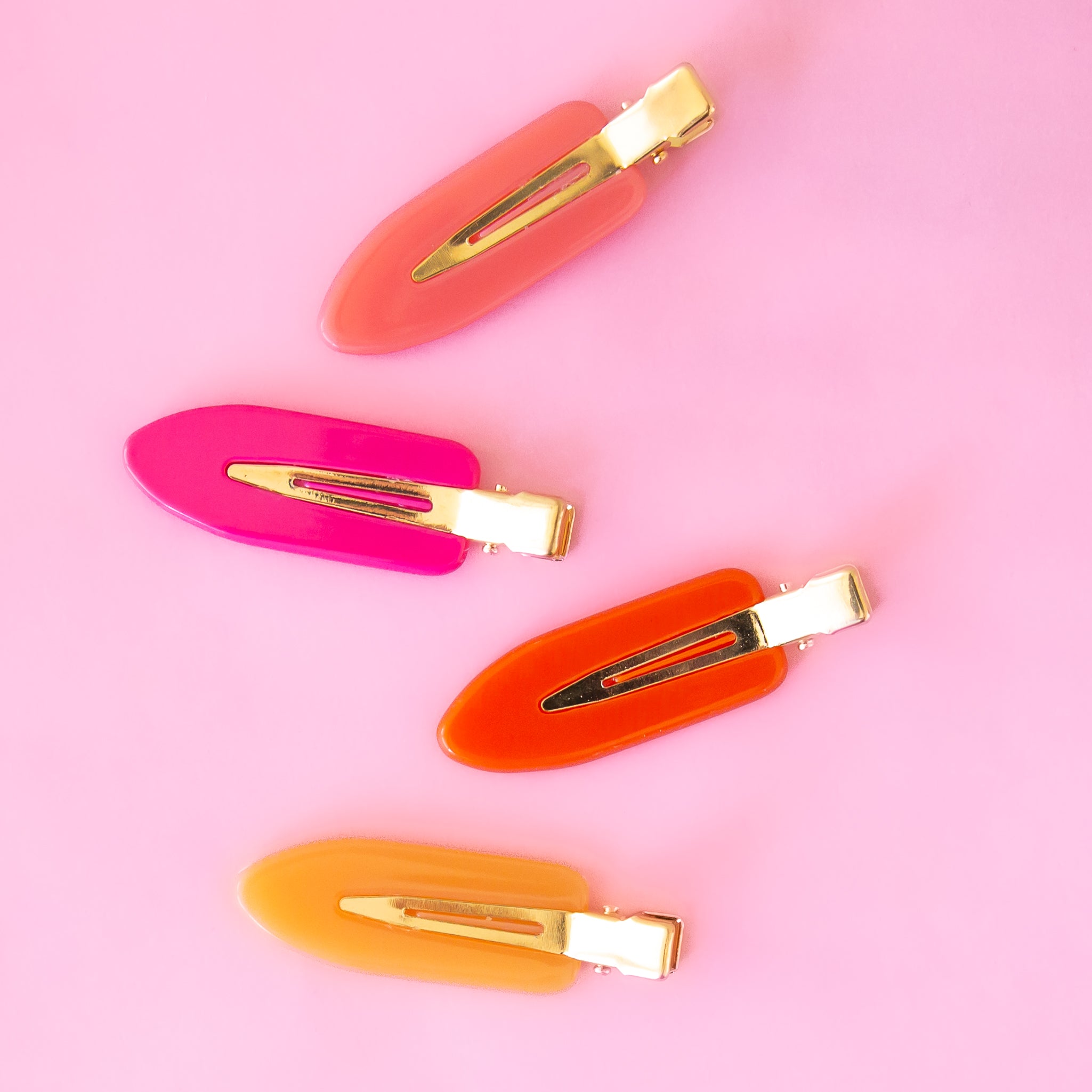 Four vibrant colored creaseless hair clips in orange, pink and yellow shades. 