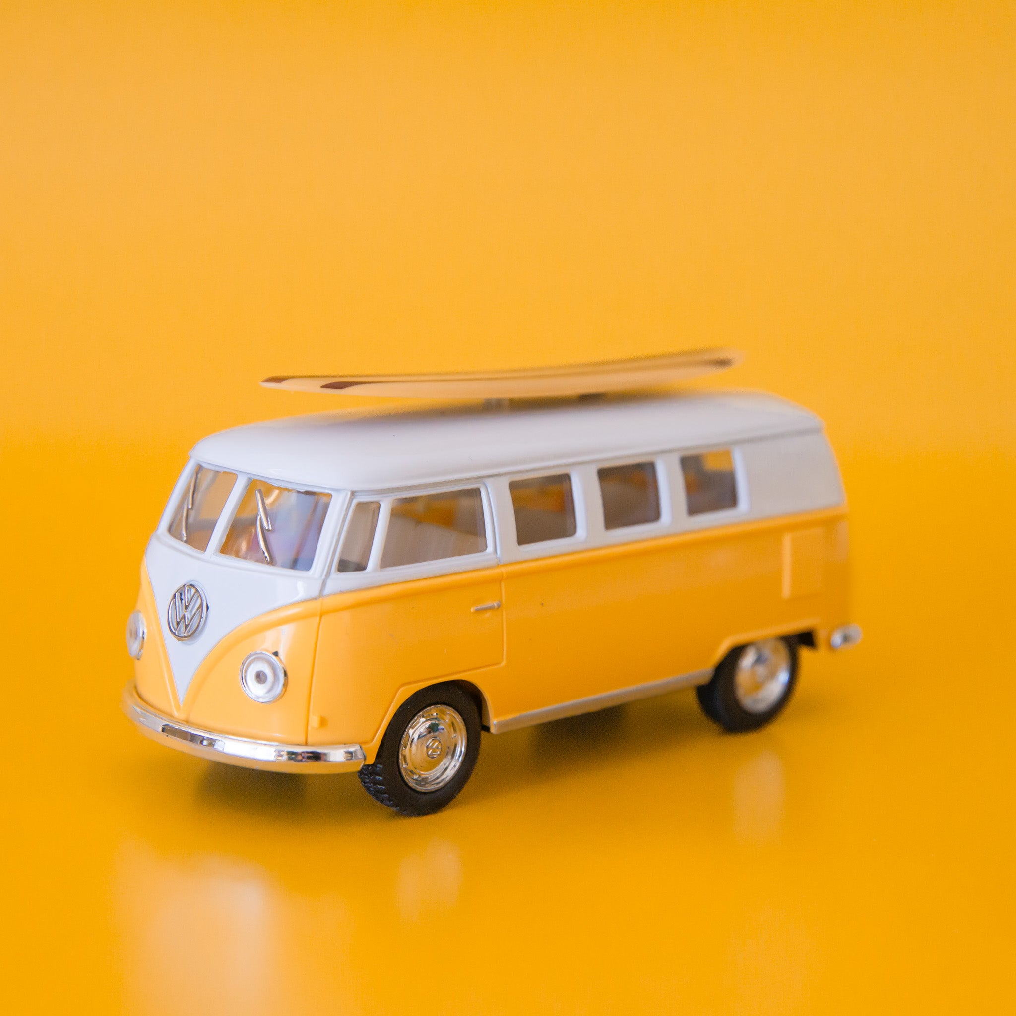 A volkswagen bus replica toy with a surf board on the top. 