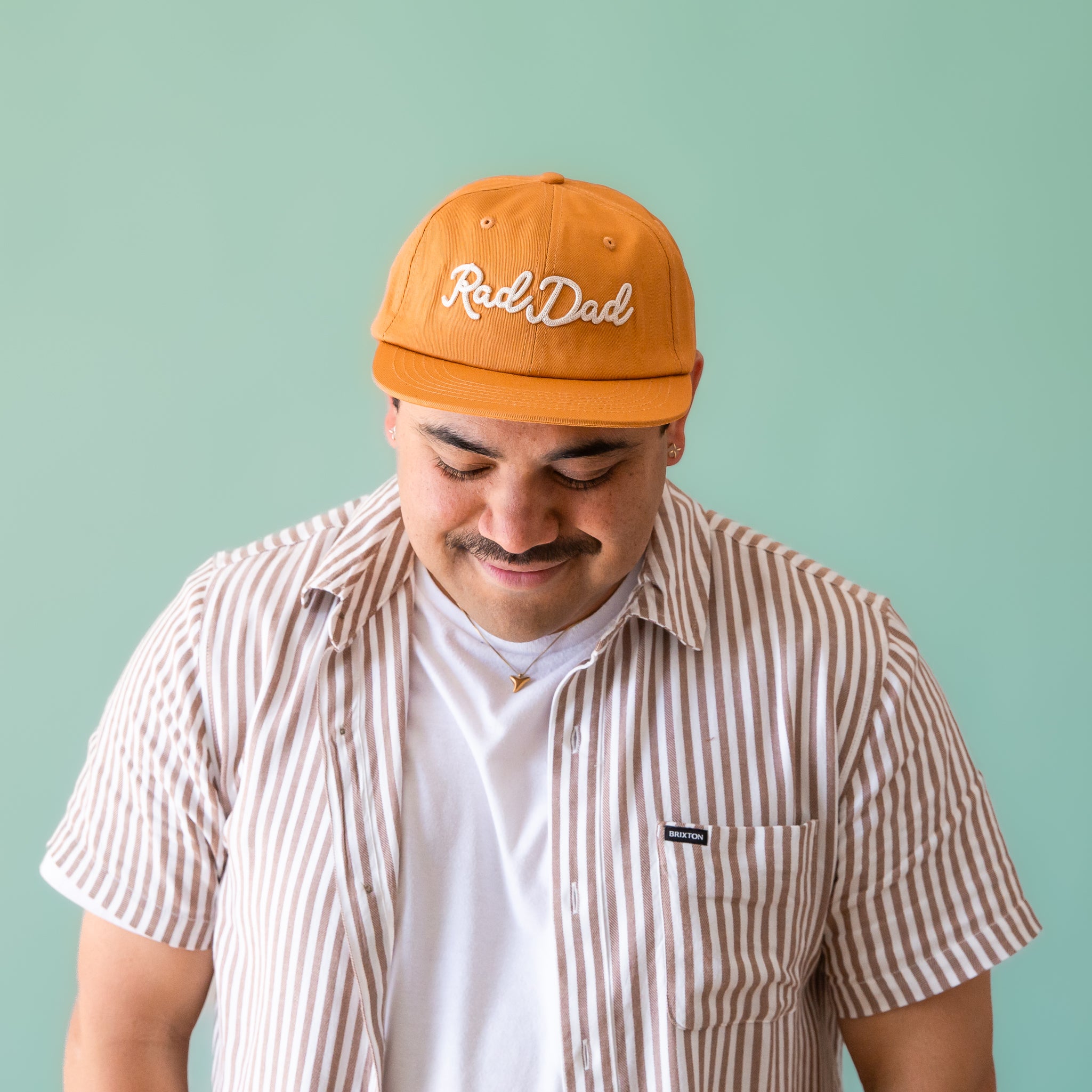 A flat brimmed burnt orange had with white embroidering that reads, &quot;Rad Dad&quot;.