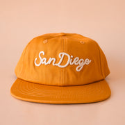 A burnt orange flat brim hat with ivory embroidered text that reads, "San Diego". 