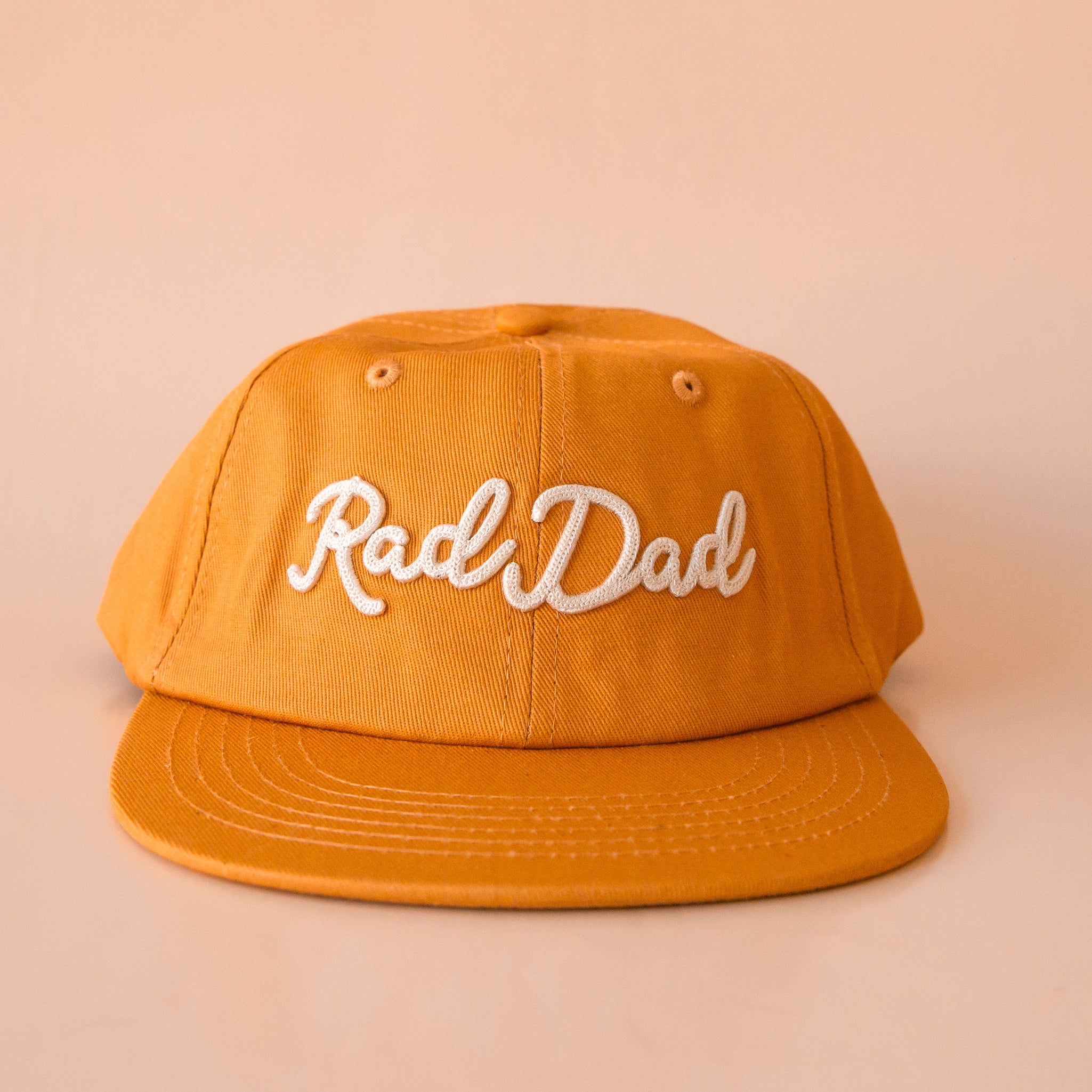 A flat brimmed burnt orange had with white embroidering that reads, "Rad Dad".