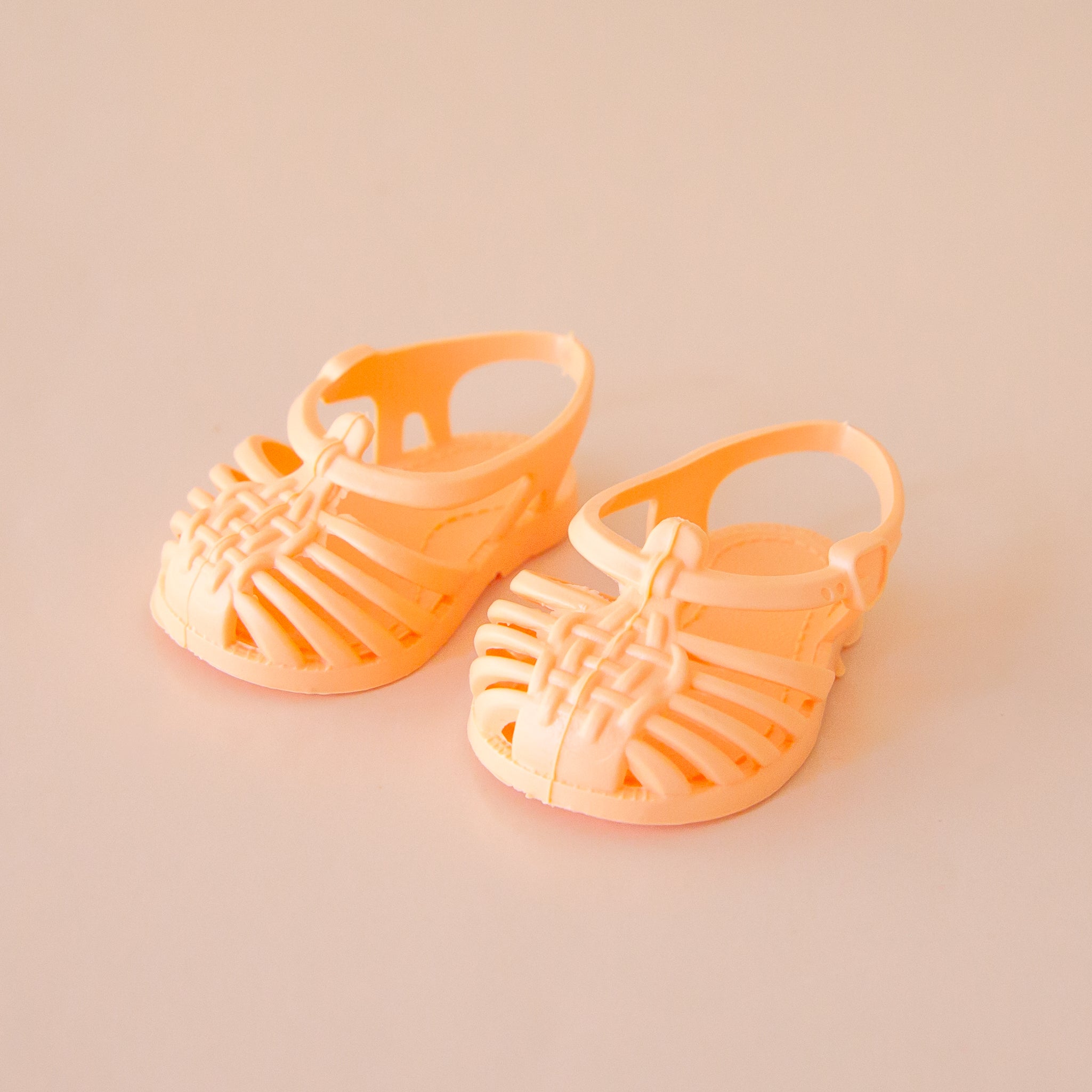 A pair of doll sandals in a peachy orange shade. 