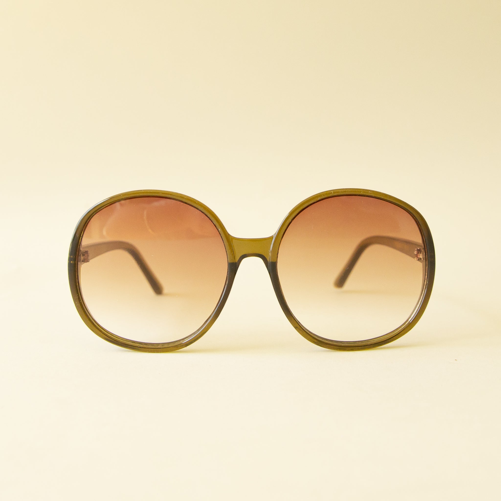 A green translucent pair of round oversized sunglasses with a light brown / pink lens.