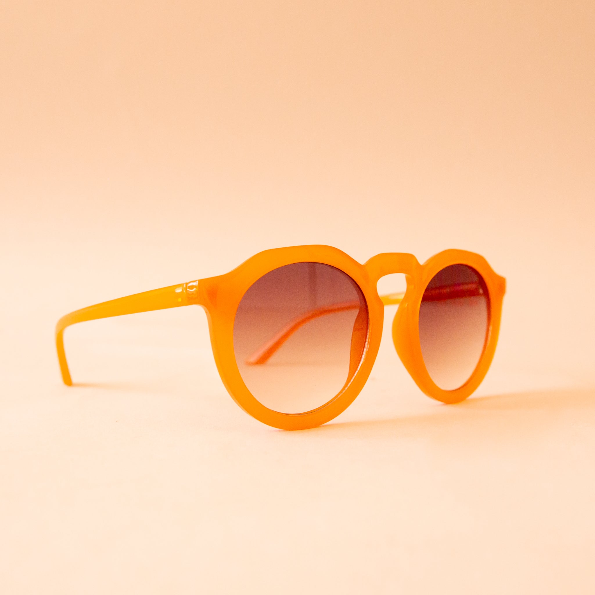 A pair of orange round sunglasses with a brown gradient lens.