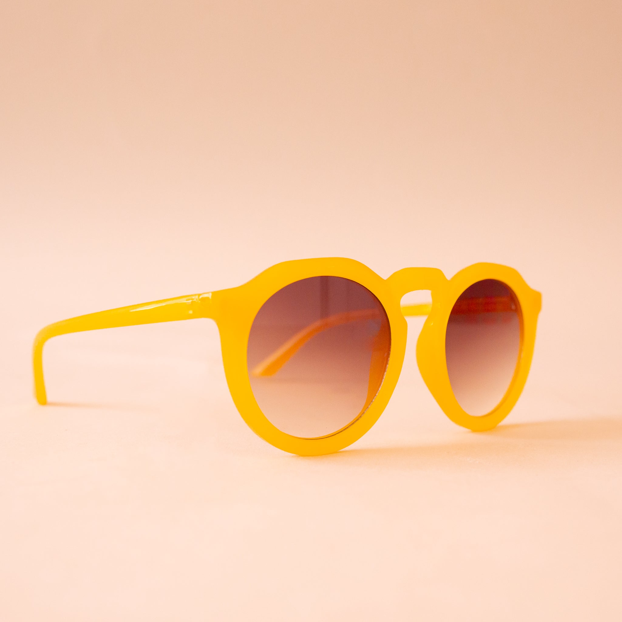 A pair of yellow round sunglasses with a brown gradient lens.