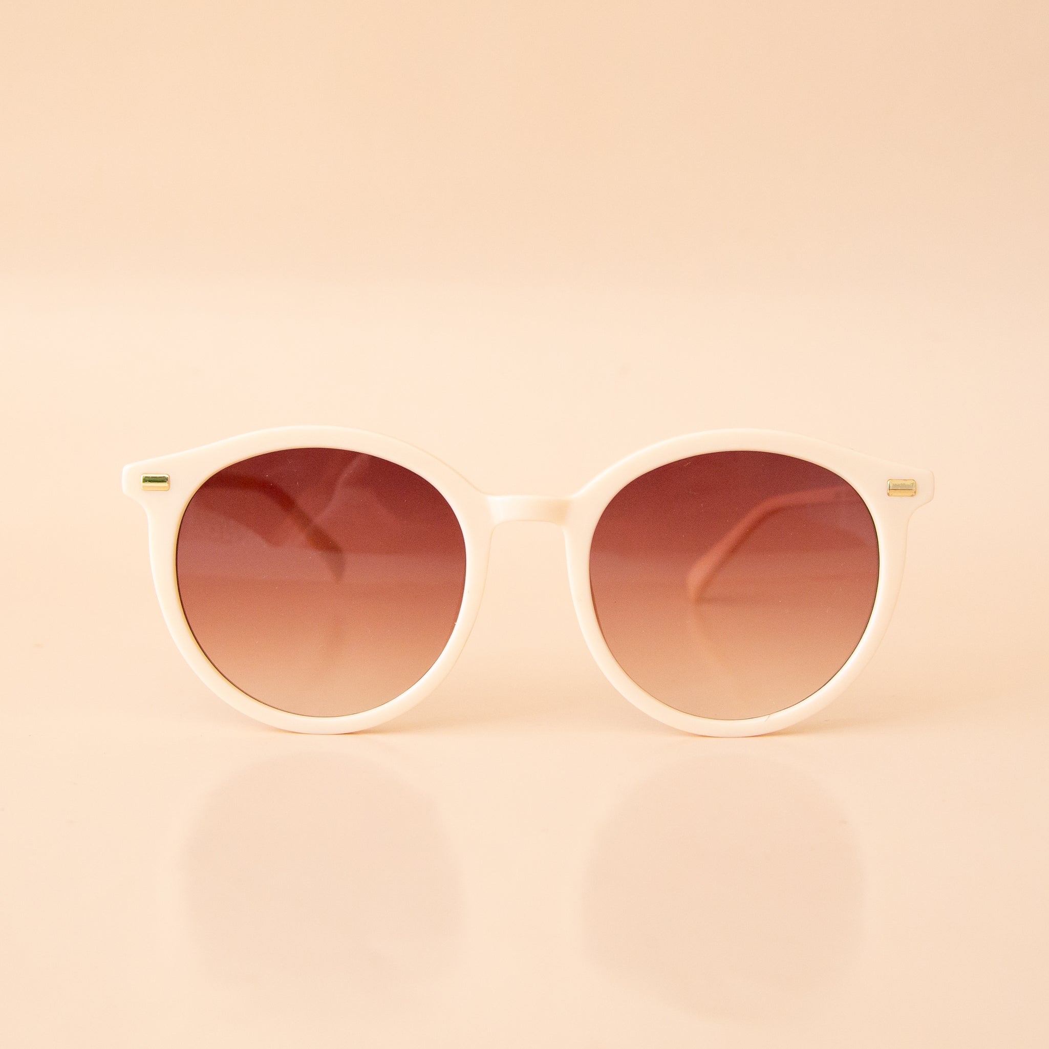 A white pair of rounded sunglasses with a brown lens. 