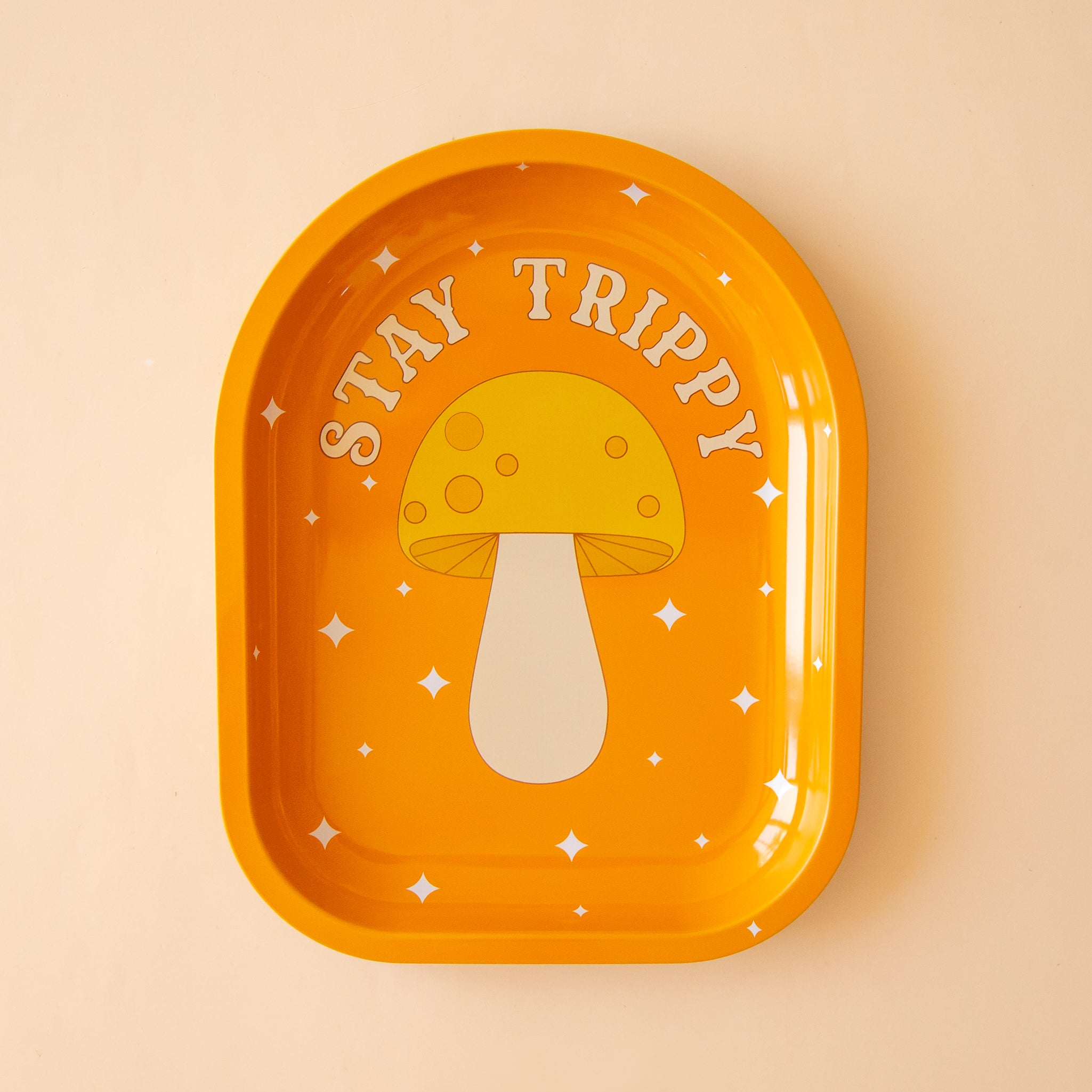 An arched shape orange metal tray with a mushroom graphic and text above that reads, &quot;Stay Trippy&quot;. 