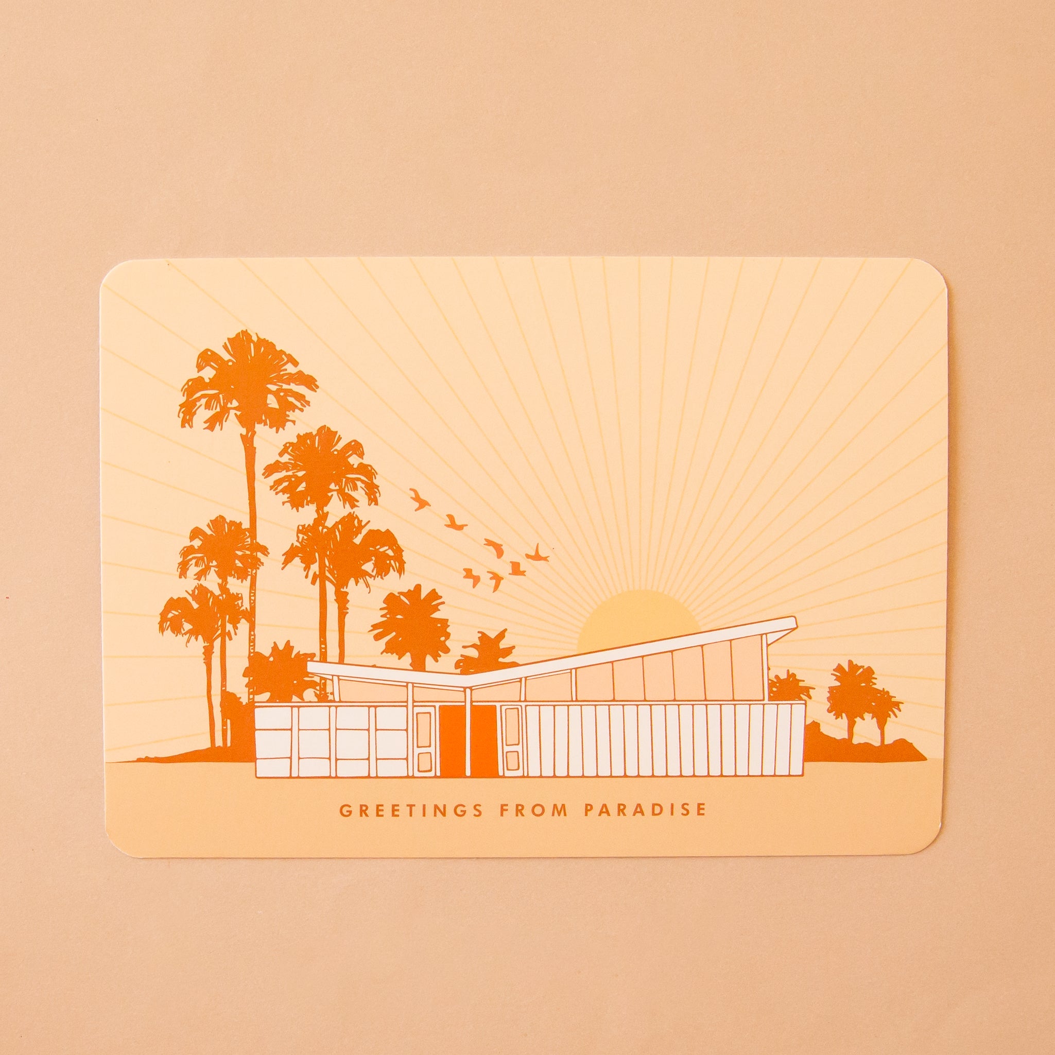 A light pink postcard with a mid century home along with palm trees and a rising sun. The text on the bottom says, "Greetings from paradise".