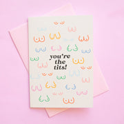 The text reads, "You're the tits!" on a white card with different colored breast illustrations that vary in all different sizes and shapes. The colors include light blue, dark blue, green, mustard, red and pink! 