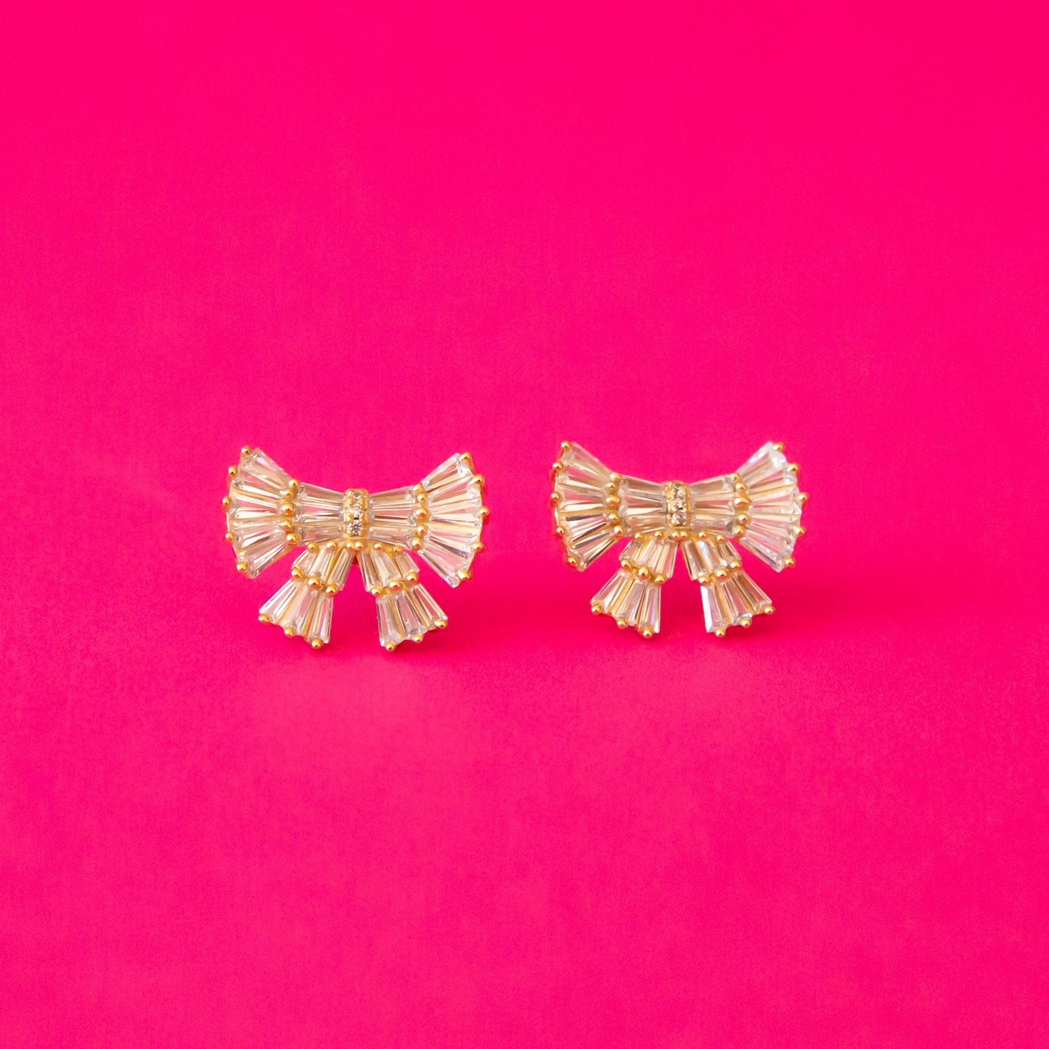 A pair of gold and pink bow shaped earrings with small baguette shaped stones.