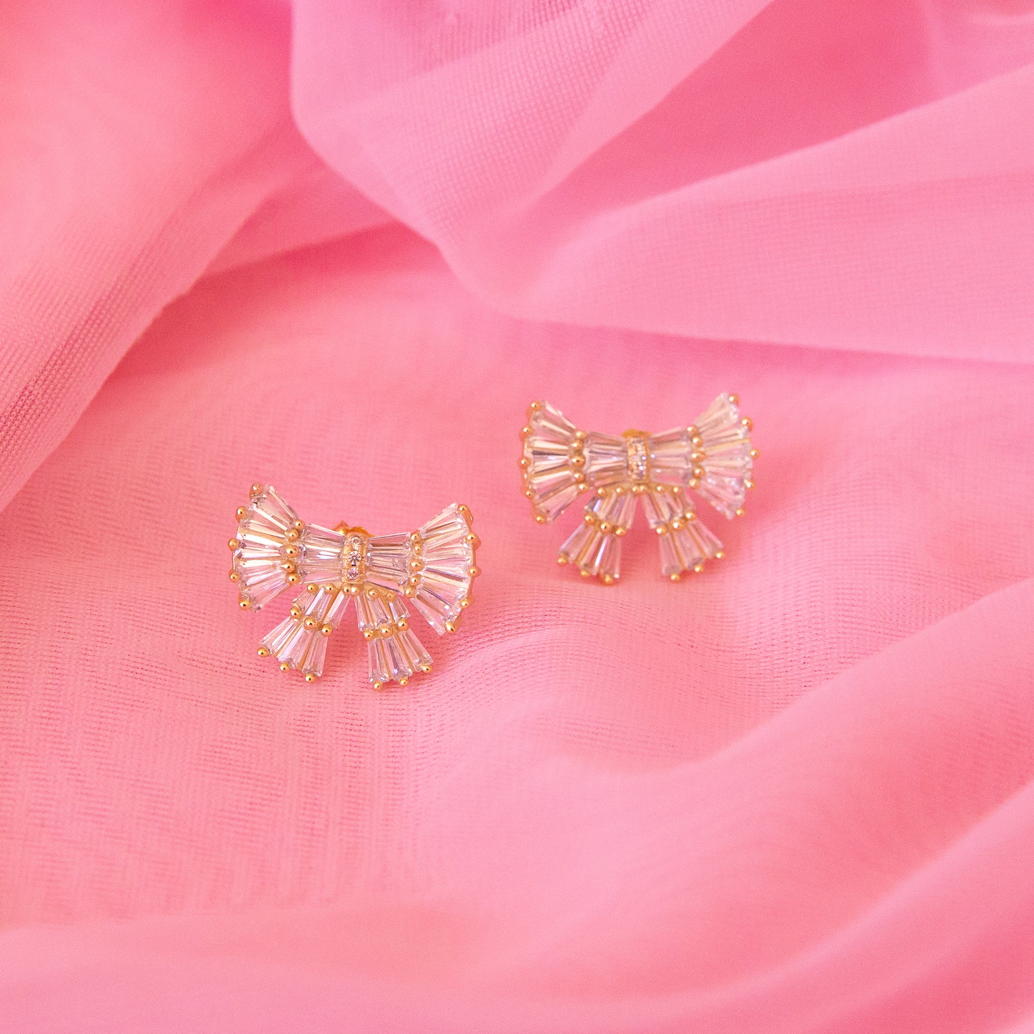 A pair of gold and pink bow shaped earrings with small baguette shaped stones. 