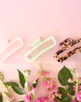 On a light pink background is three of the rectangle claw clips in a light tortoise shade, a pearly white and a light mint green. 