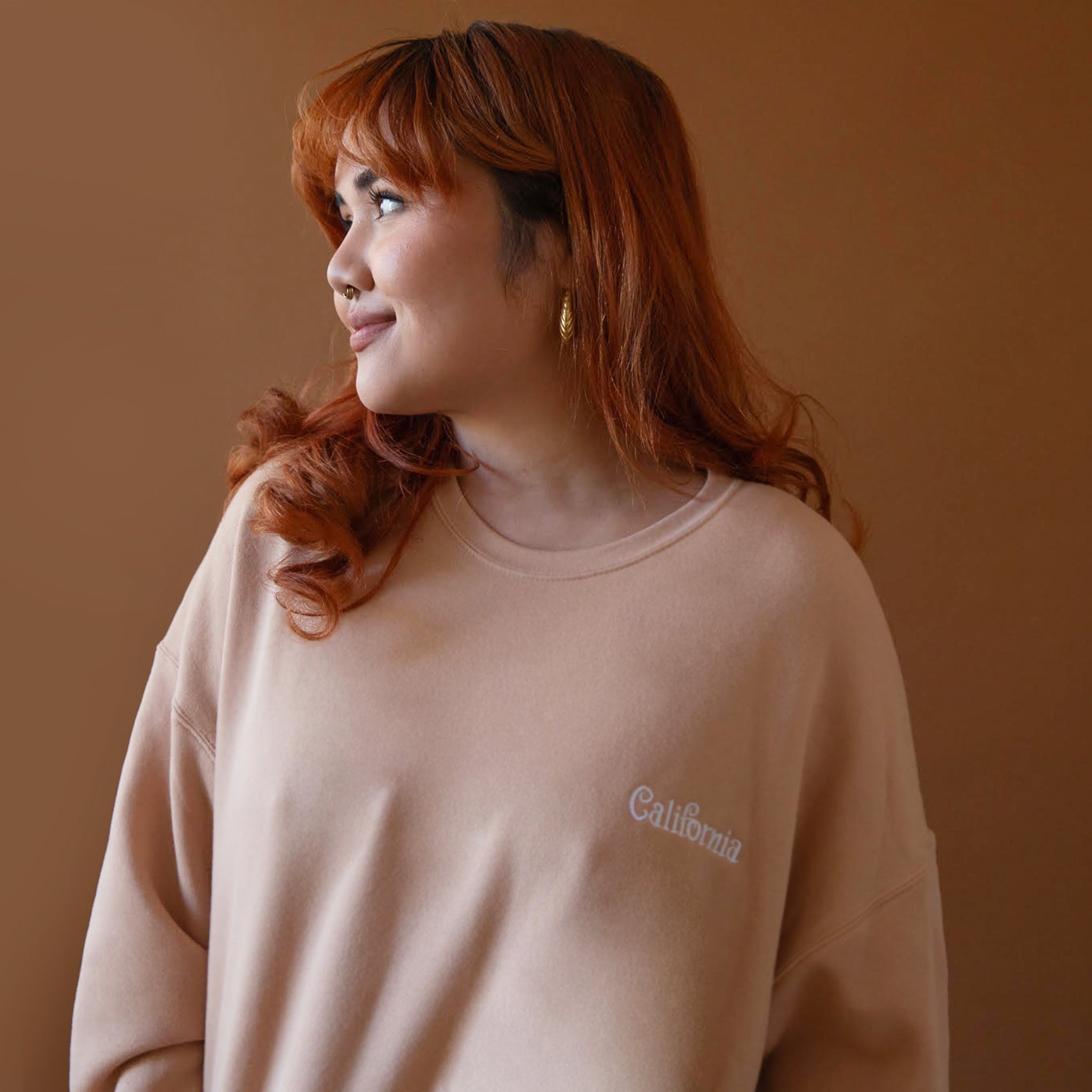 On a brown background is a peachy fleece pullover with white "California" embroidering.