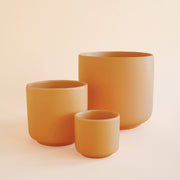 On an ivory background is three u-shaped ceramic planters in an orange terracotta color with a smooth matte finish. 