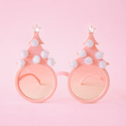 On a pink background is a pair of holiday glasses with tree shapes and six white pom poms and a star on top.