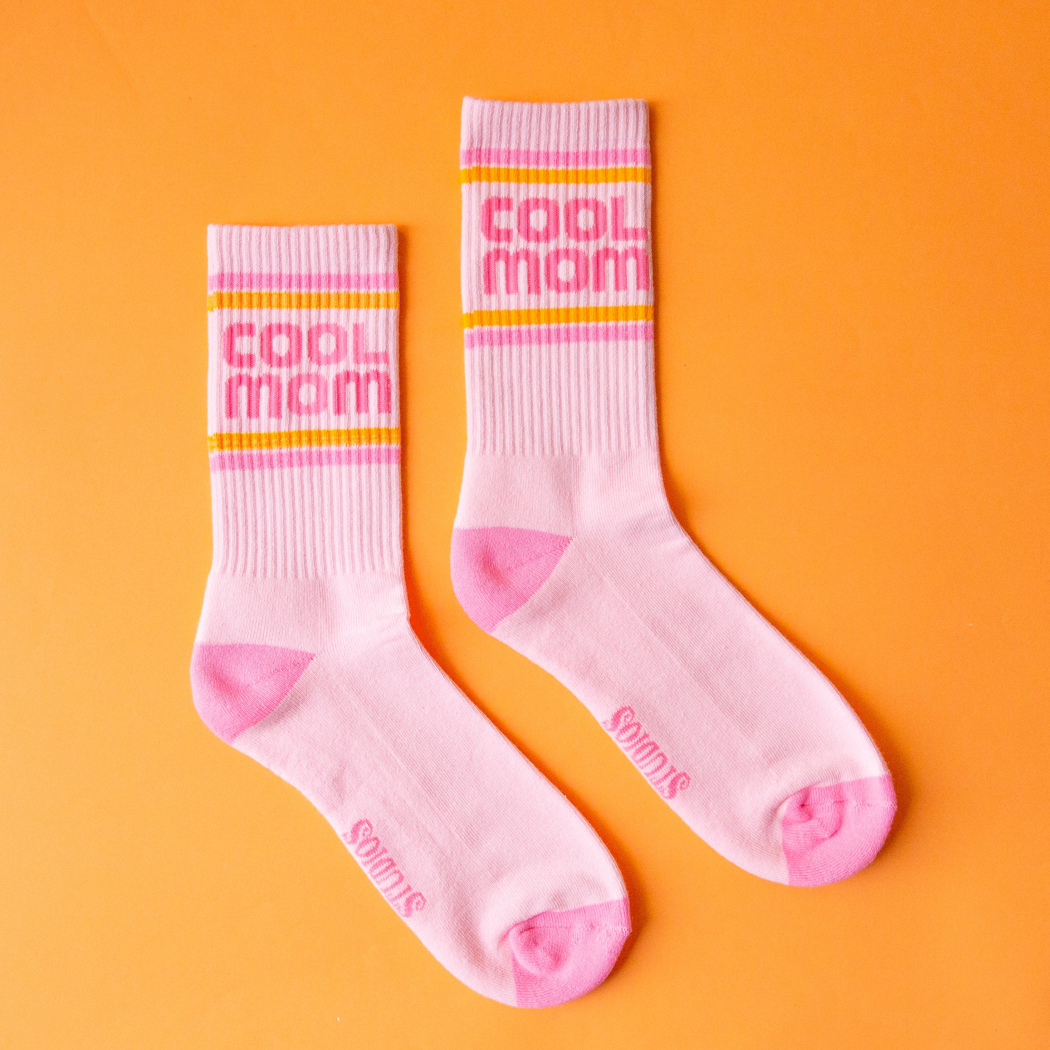 A pair of crew socks with pink and orange stripes and pink text that reads, &quot;cool mom&quot;.