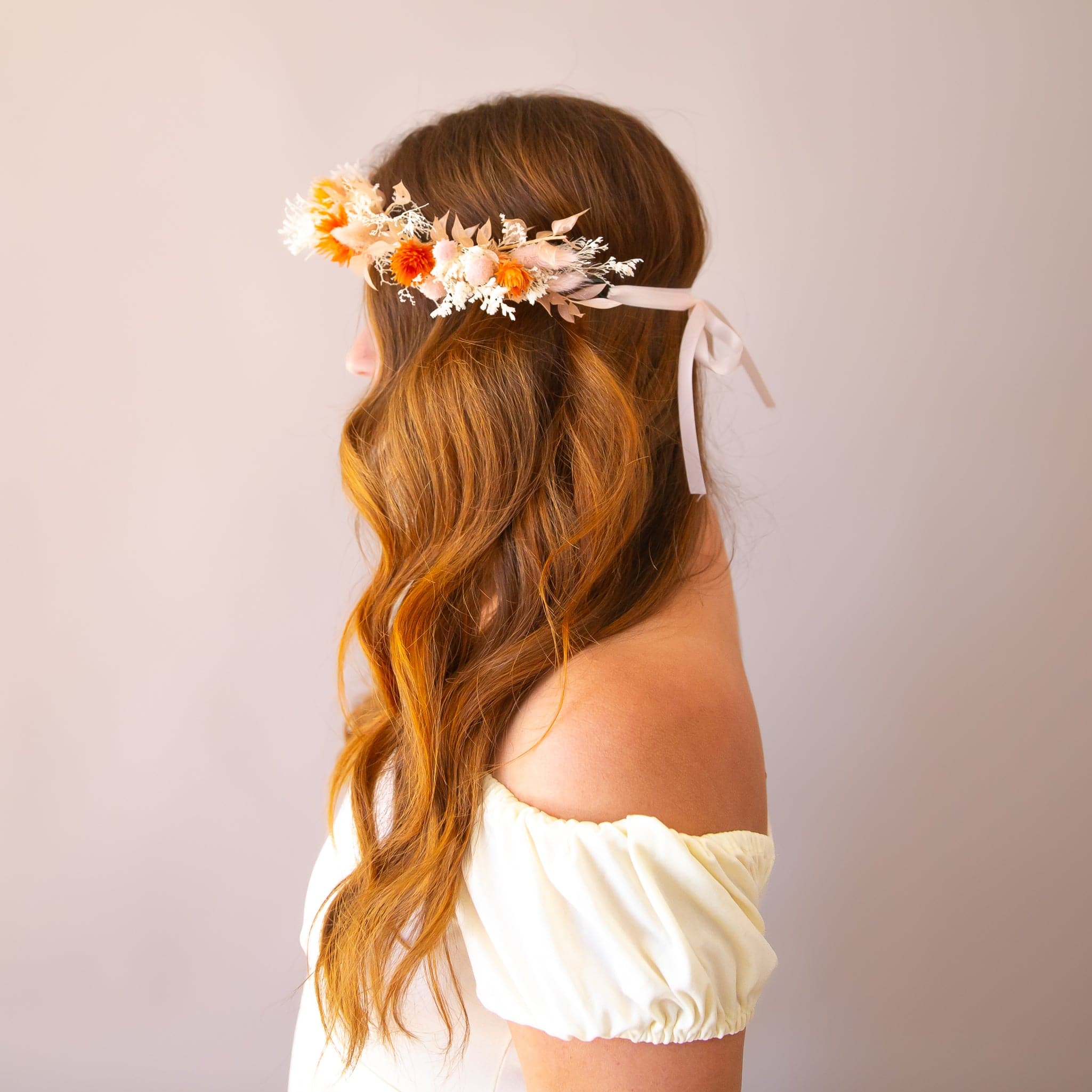 A flower crown made up of orange and neutral dried florals with a ribbon tie detail on the back. 