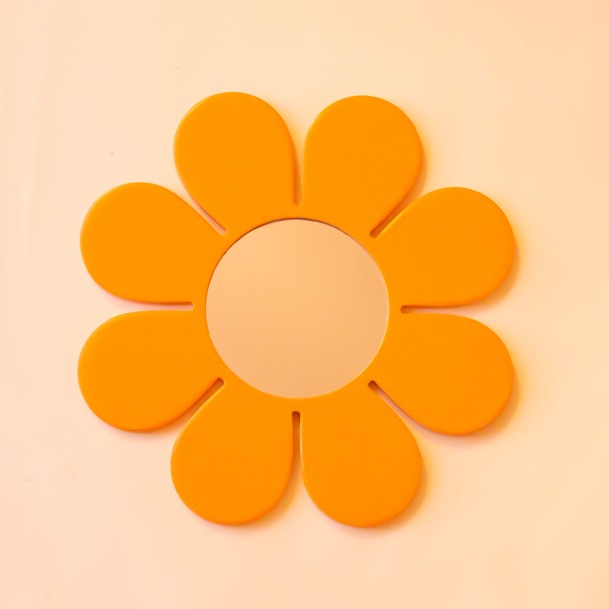 A mustard yellow wood mirror in the shape of a daisy. 