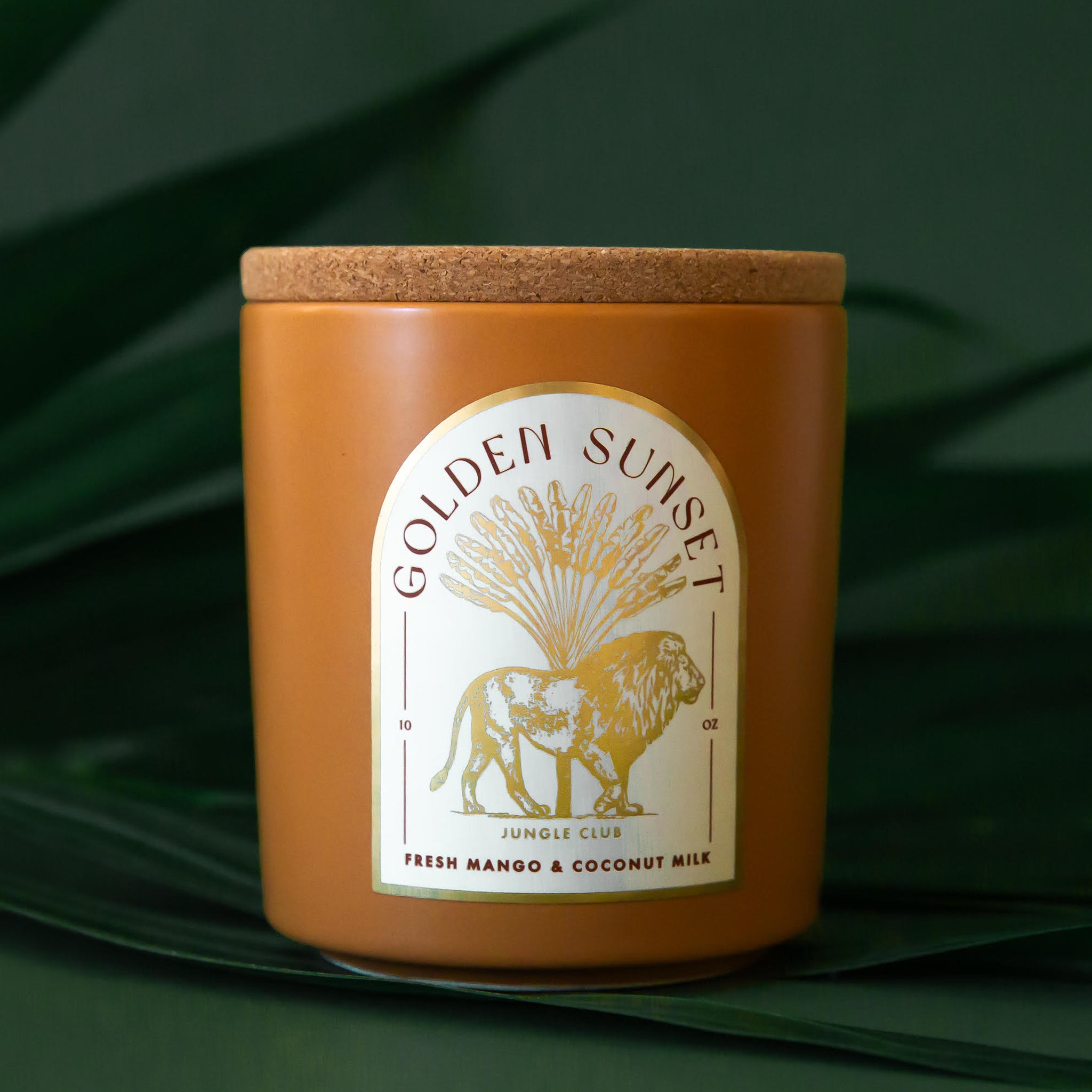 An orange candle with an arched label with a lion graphic and text above that reads, 'Golden Sunset'. 