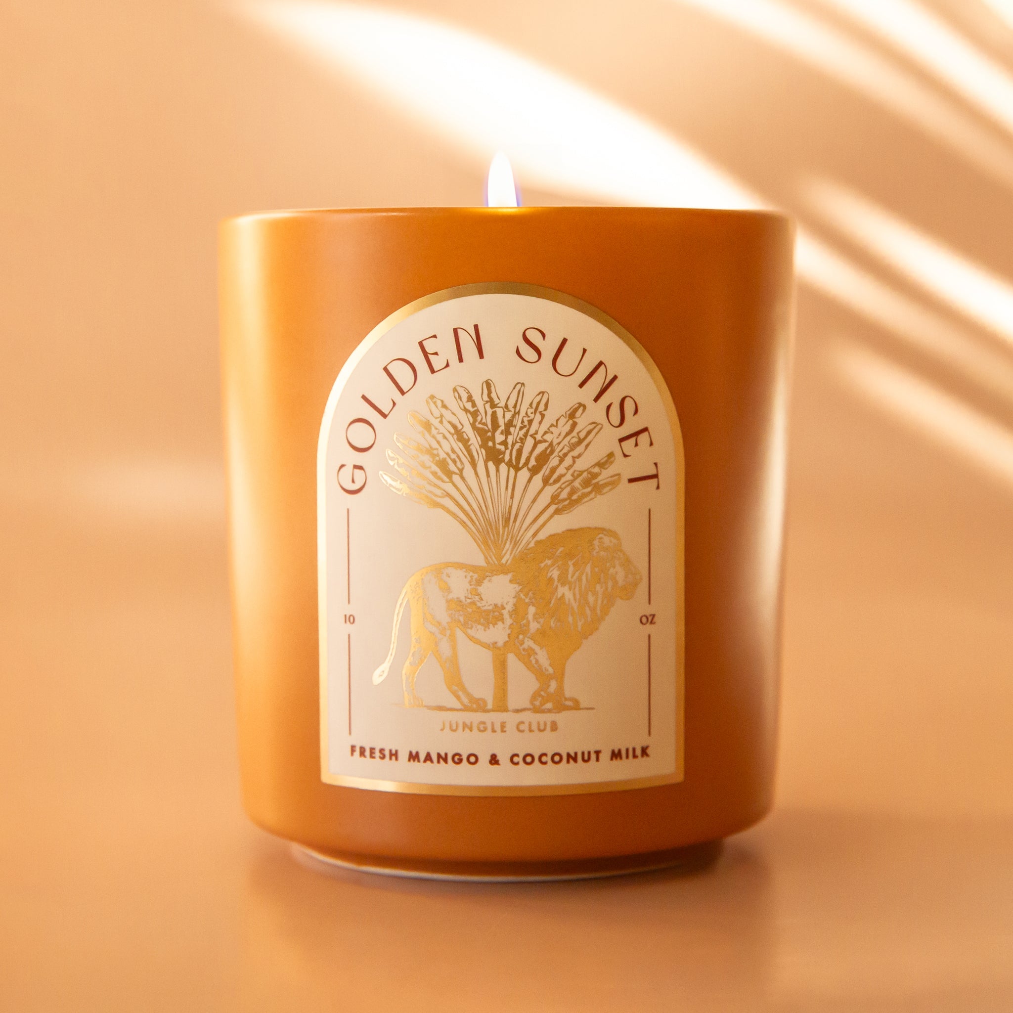 An orange candle with an arched label with a lion graphic and text above that reads, &#39;Golden Sunset&#39;. 