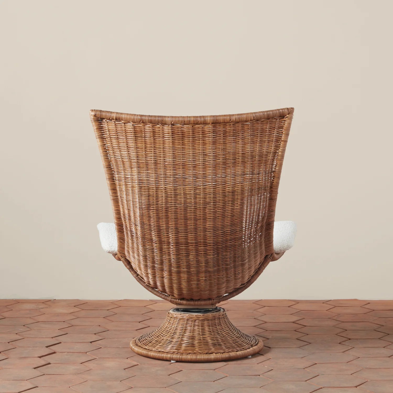 A woven chair with a squared top edge that is curved along the back with an ivory boucle cushion. 