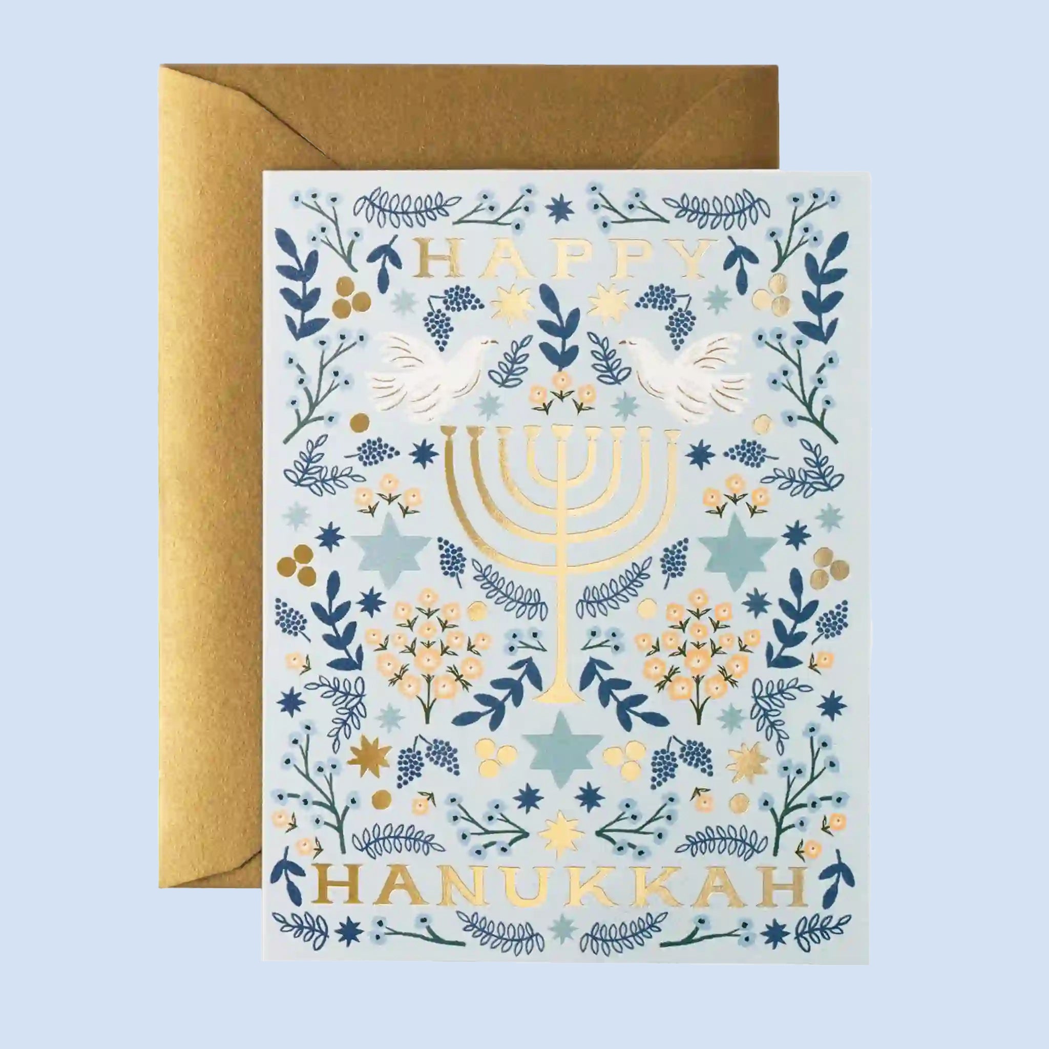 On a neutral background is a blue and white greeting card with gold fold text that reads, "Happy Hanukkah" along with a menorah graphic. 