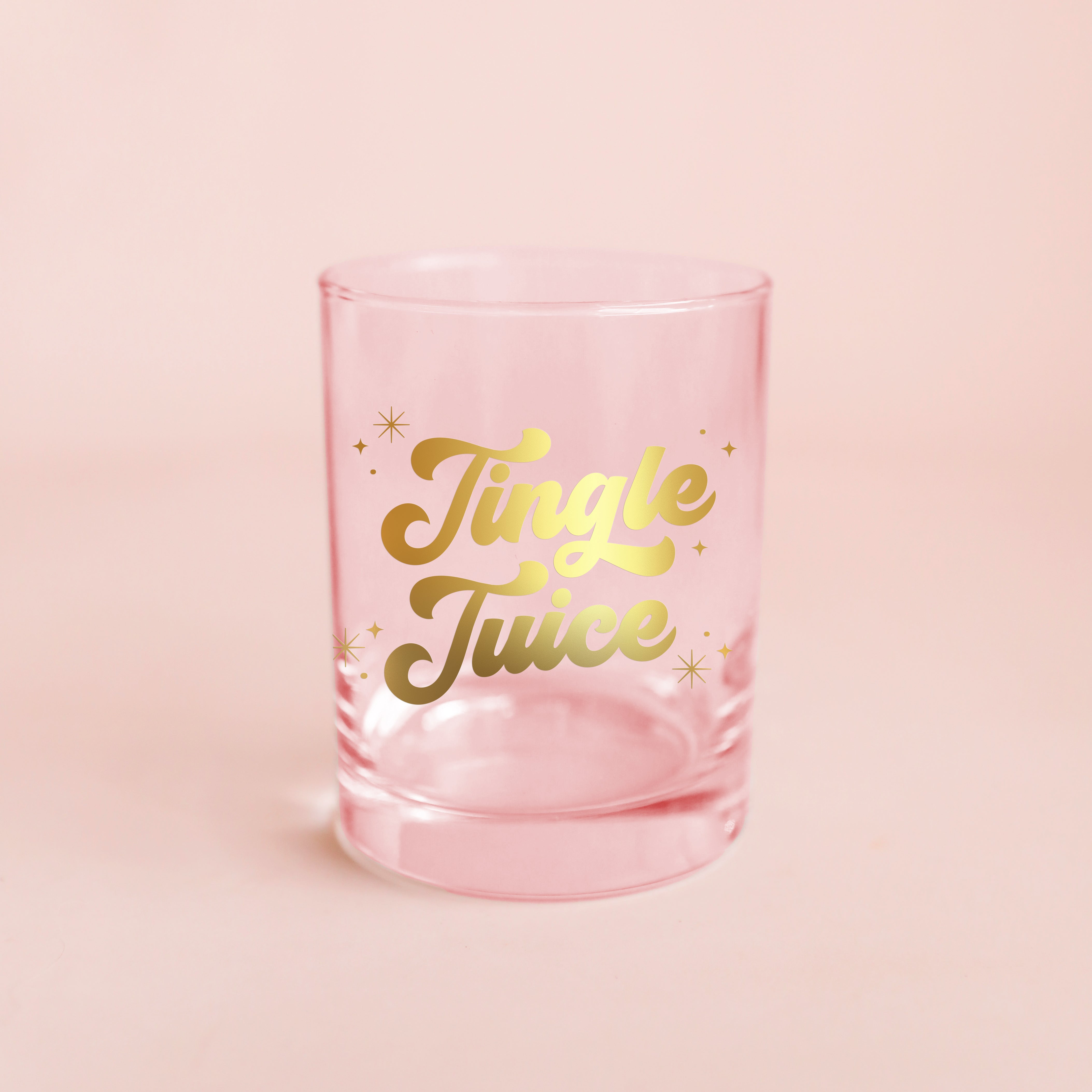 Glass cup with gold lettering is shown against a pink background that reads, &#39;Jingle Juice&#39;. 