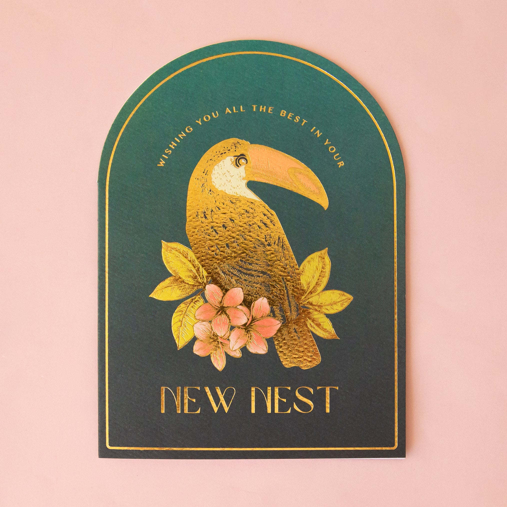 An arched shaped teal blue card, with a gold foiled illustration of a toucan bird and text above and below that reads, "Wishing You All The Best In Your New Nest"