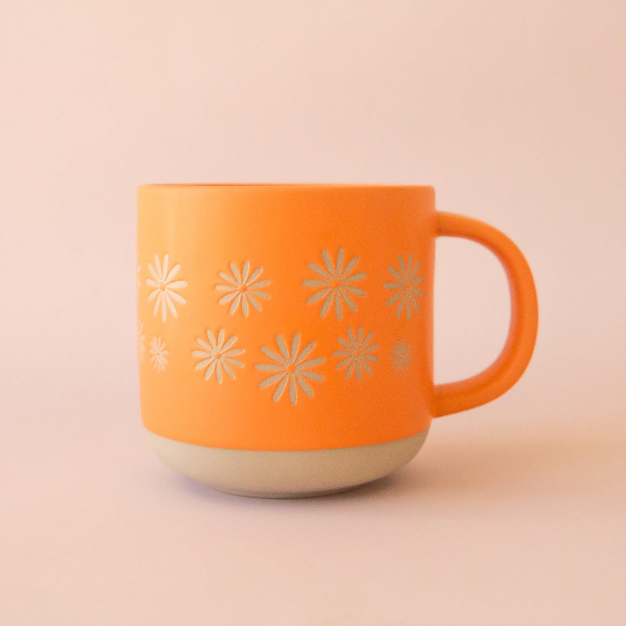 A ceramic yellow / orange mug with small pinwheel daisy flower shapes around the center. 