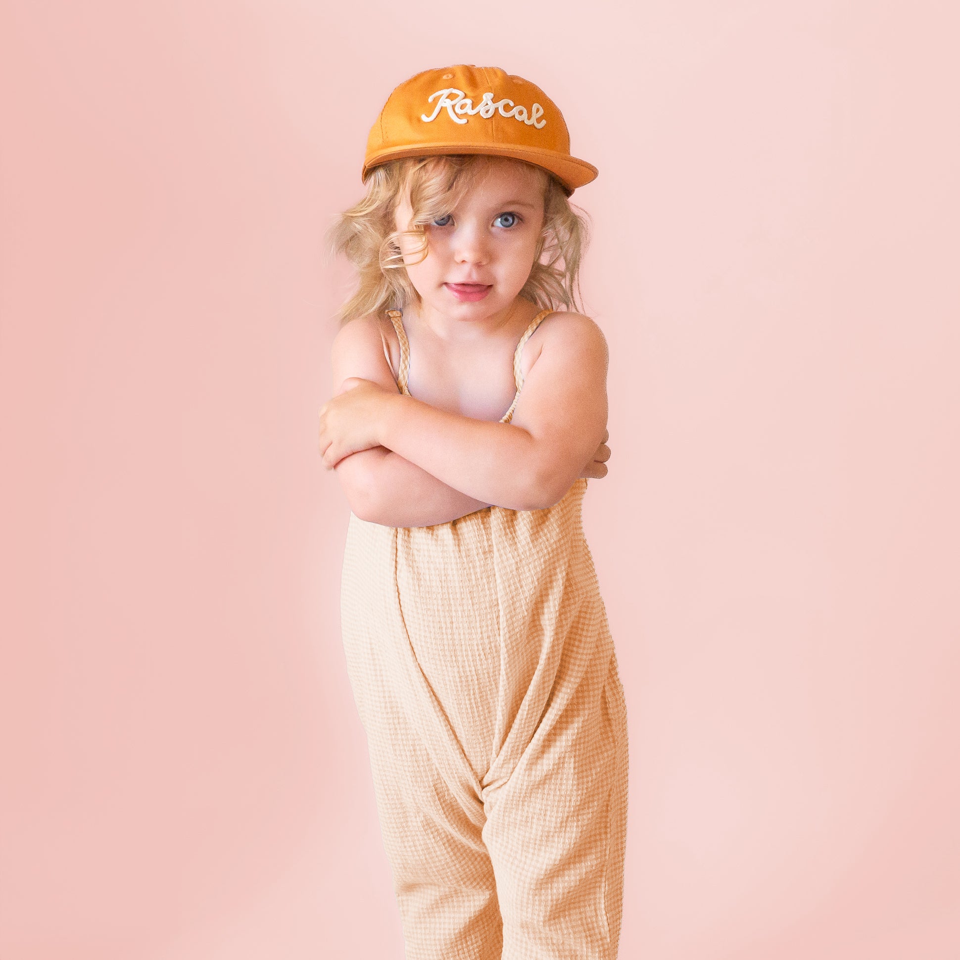 A burnt orange flat brimmed hat with white embroidered text that reads, &quot;Rascal&quot;.