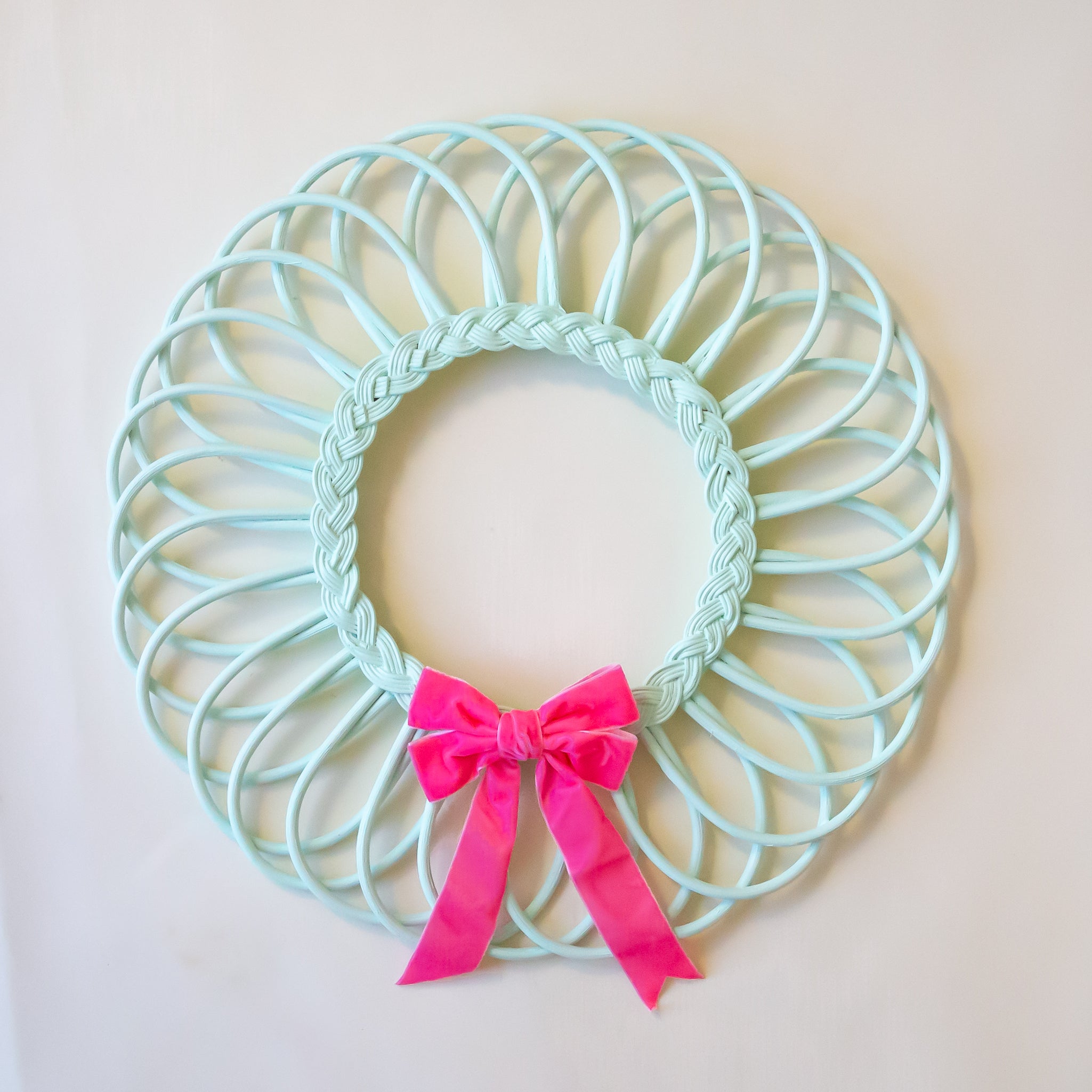 A mint green rattan wreath with a pink bow in the center. 