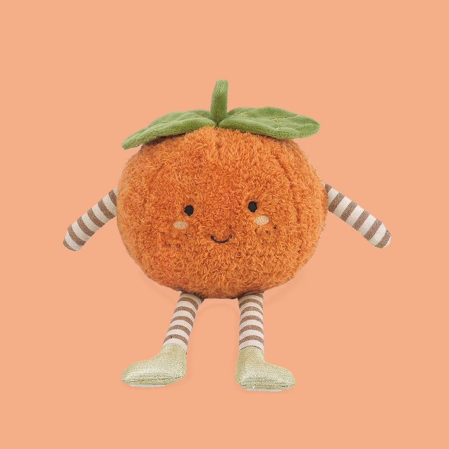 A darling little clementine orange shaped stuffed animal with a smiley face and little black eyes sits on an orange background.  the Clementine has leave on top of it's head and striped legs and arms with little gold shoes.