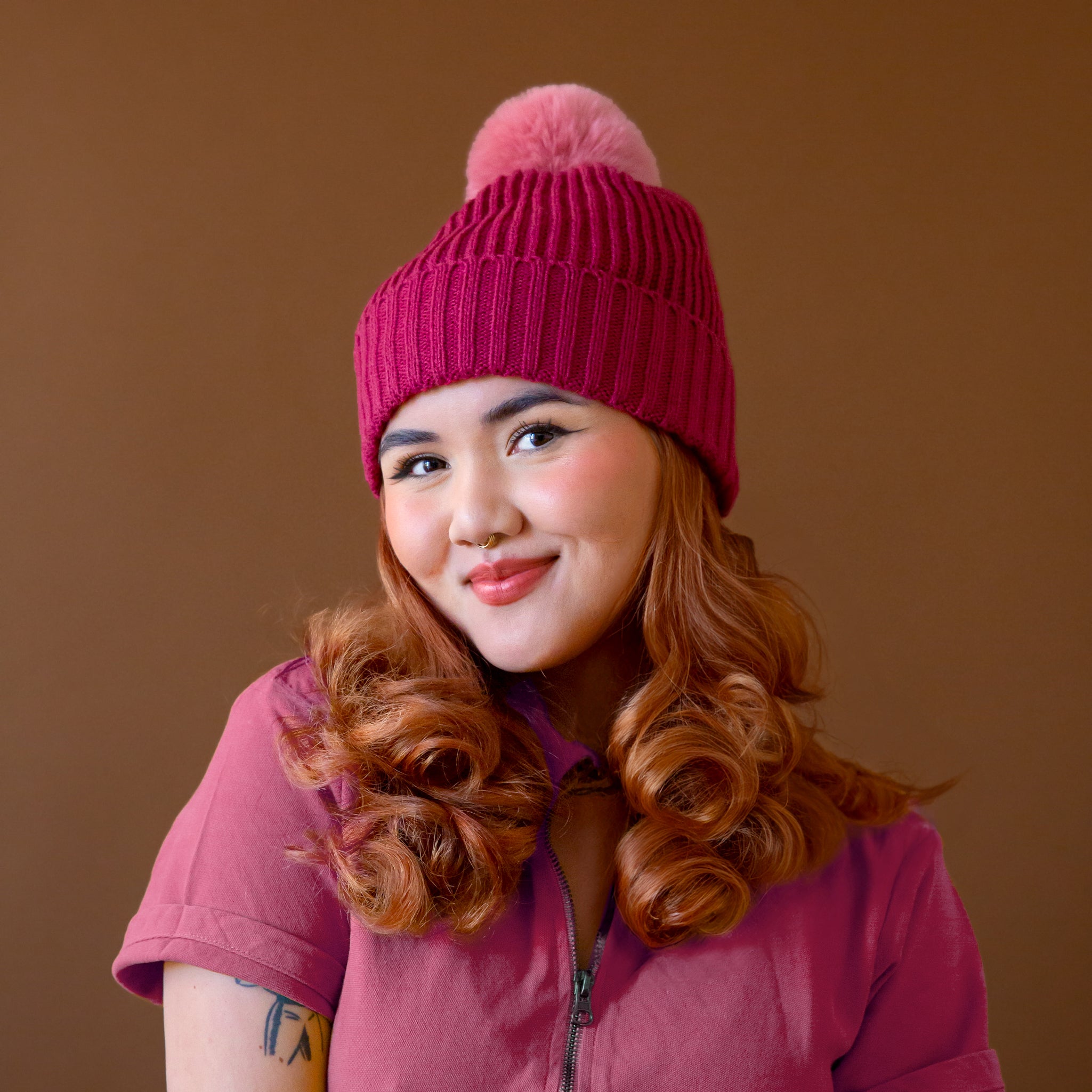 A model wearing a dark pink beanie with a lighter pink pom at the top. 