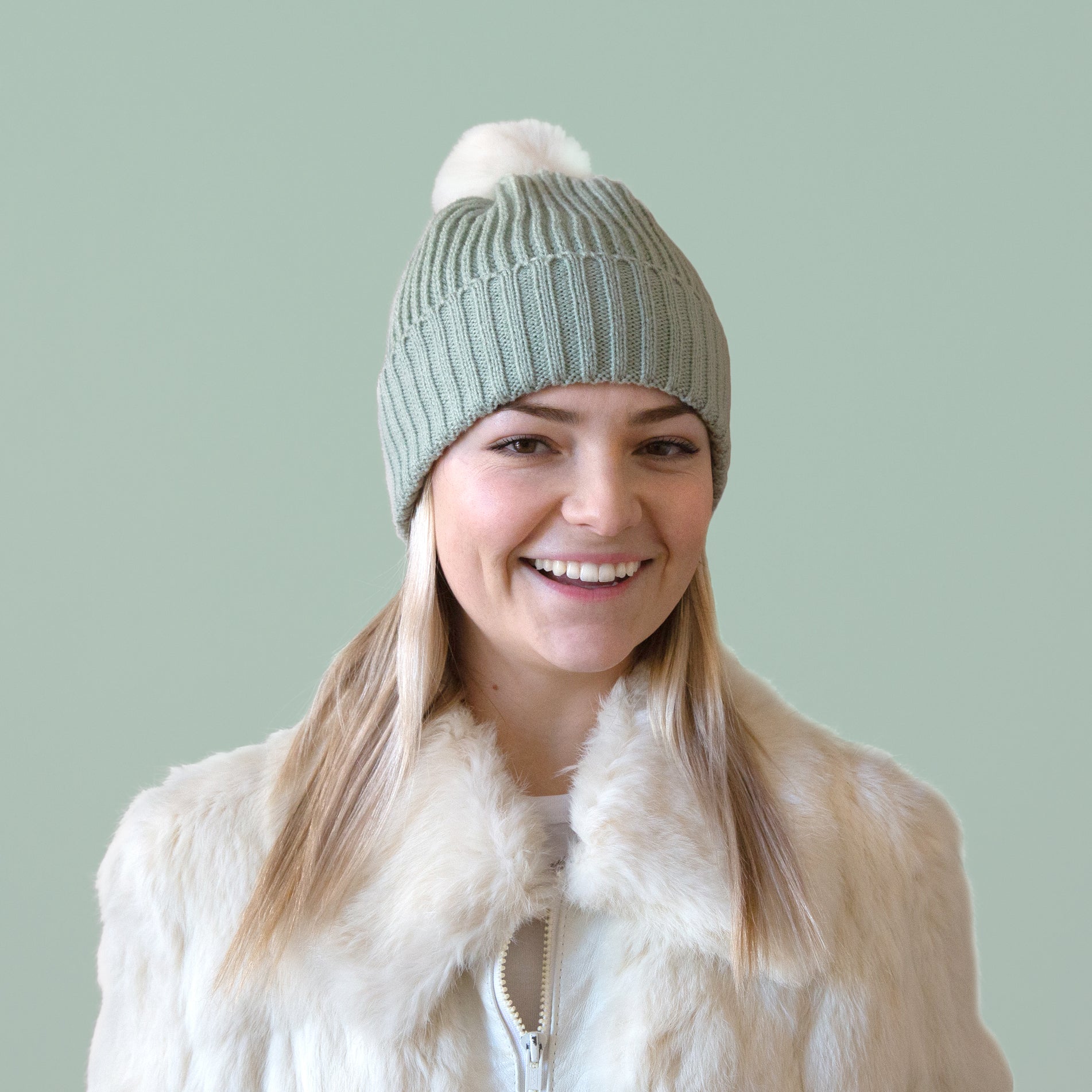 A mint green knit beanie on a model with a white pom at the top. 