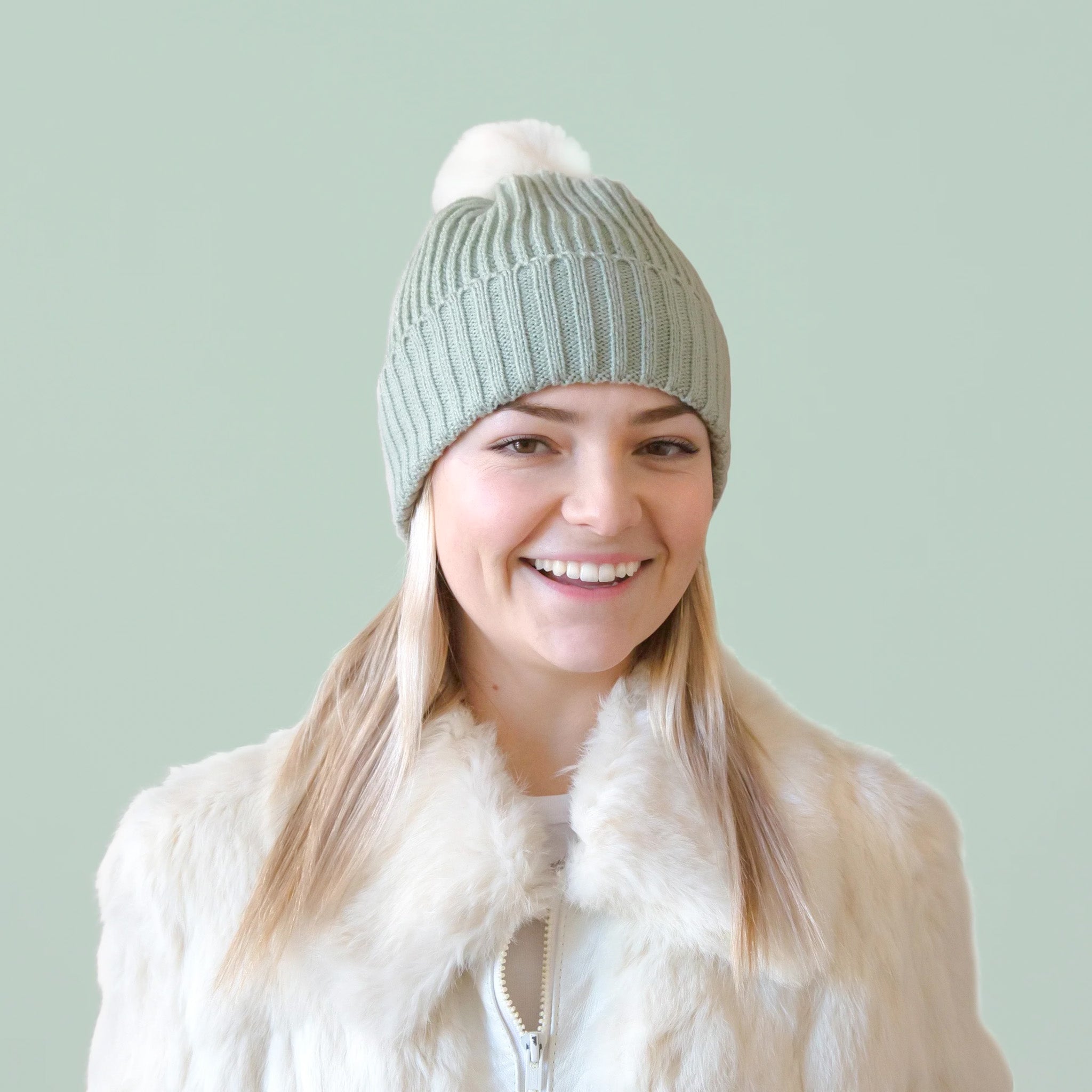 A mint green knit beanie on a model with a white pom at the top. 