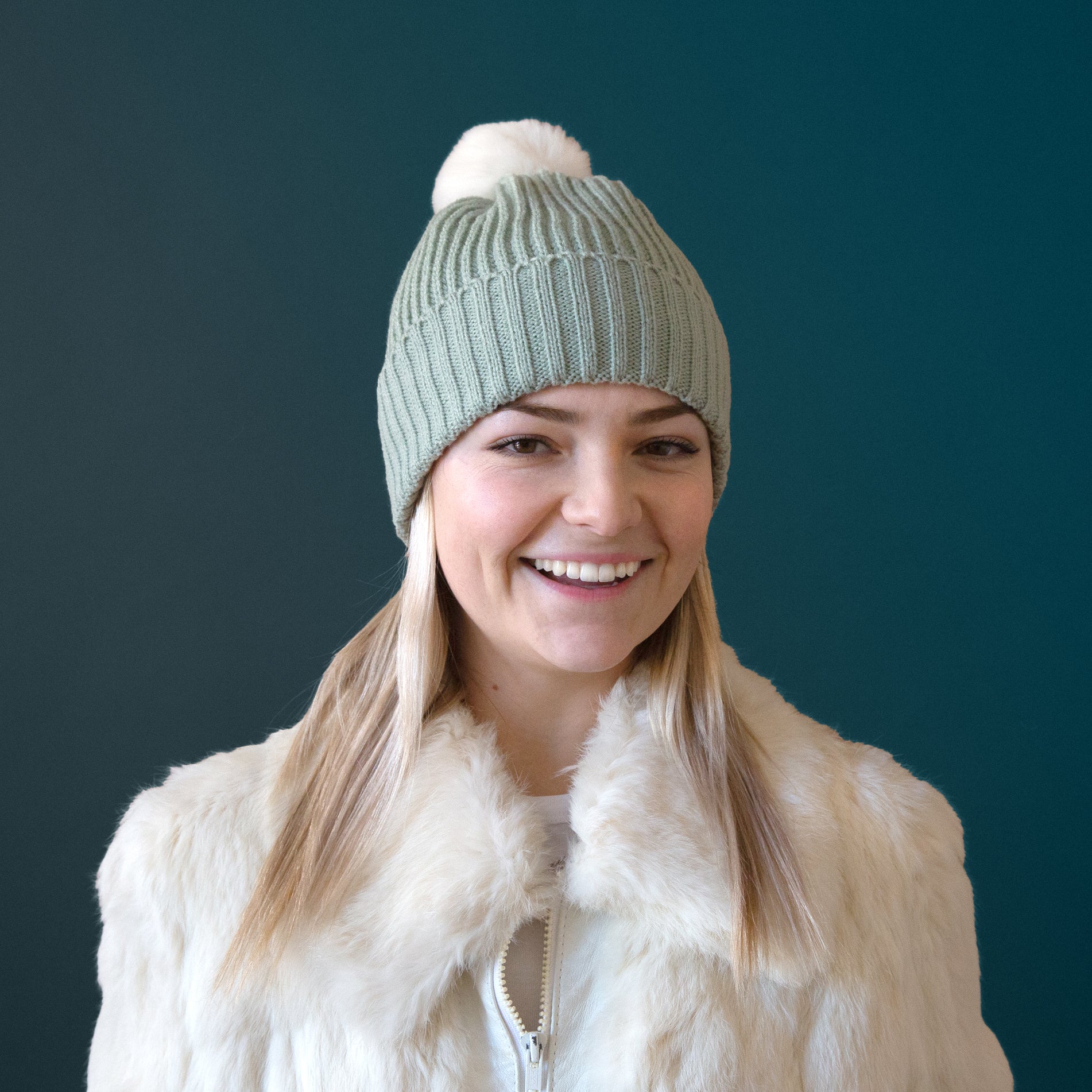 A mint green knit beanie on a model with a white pom at the top. 