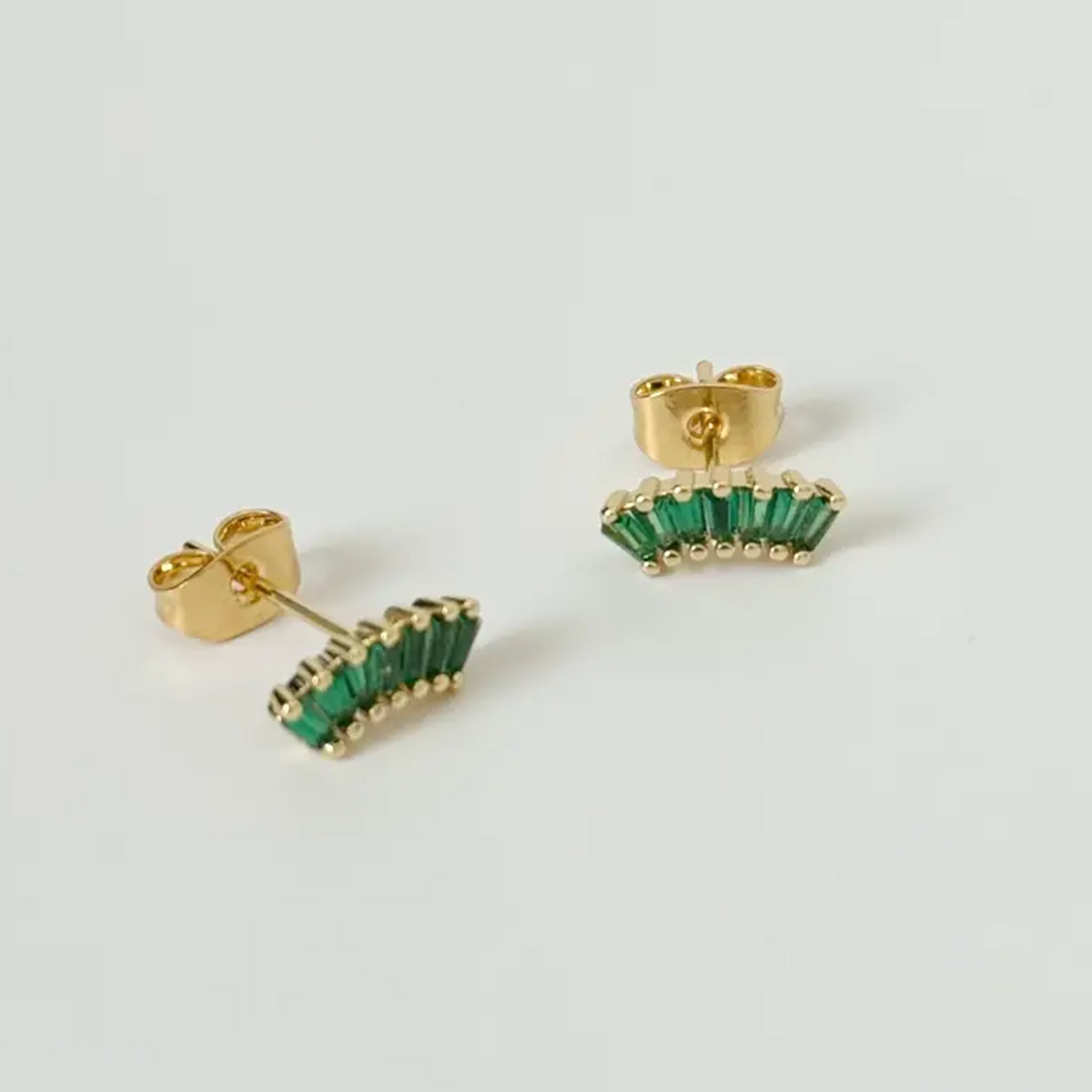 A pair of gold and emerald green stud earrings with an arch shape made of emerald shaped stones. 